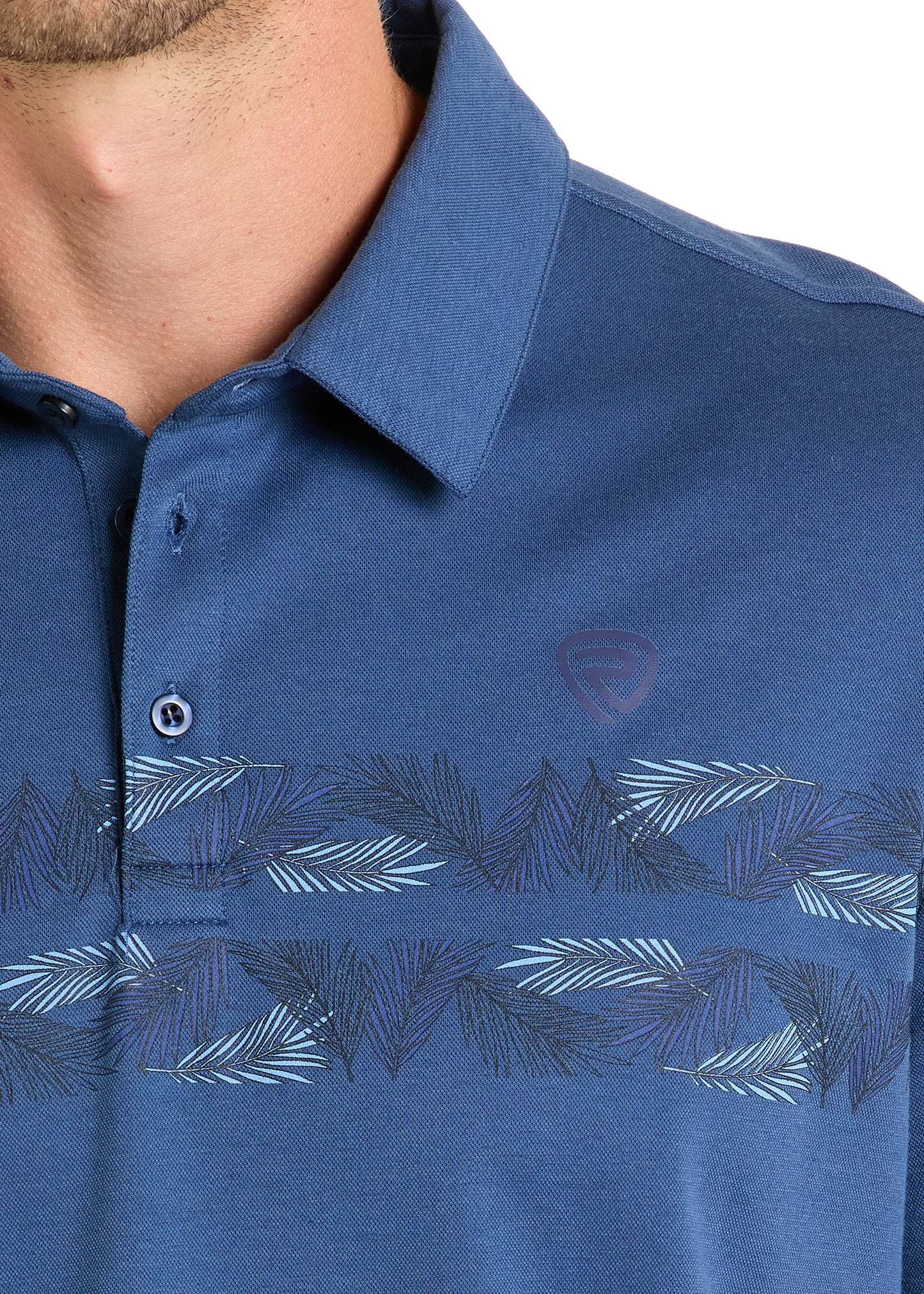 Close-up of a person wearing the Rock & Roll Denim Palm Border Polo, a blue shirt featuring a subtle leaf pattern across the chest, small logo on the left, and two buttons—one fastened—for effortless style.