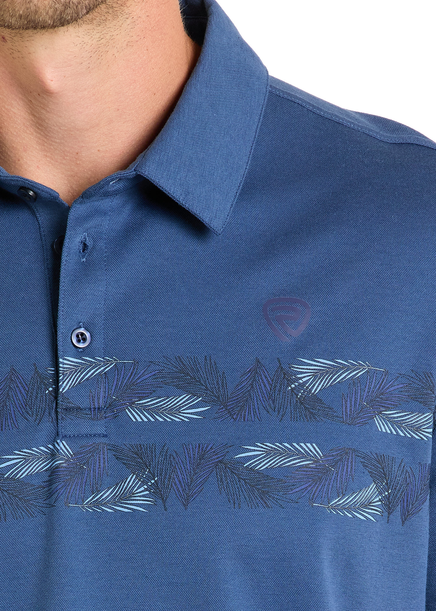 Close-up of a person wearing the Rock & Roll Denim Palm Border Polo, a blue shirt featuring a subtle leaf pattern across the chest, small logo on the left, and two buttons—one fastened—for effortless style.