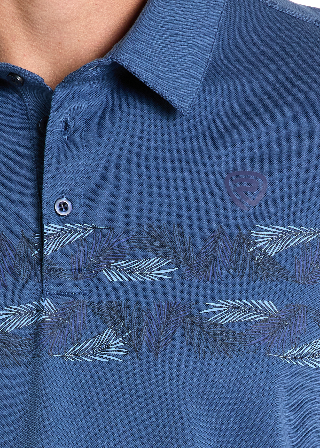 Close-up of a person wearing the Rock & Roll Denim Palm Border Polo, a blue shirt featuring a subtle leaf pattern across the chest, small logo on the left, and two buttons—one fastened—for effortless style.