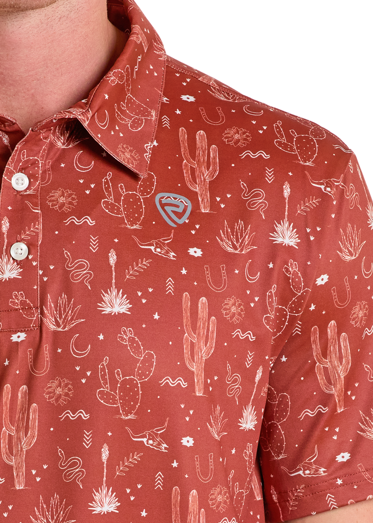 A close-up shows a person wearing the Rock & Roll Denim Western Cactus Polo, featuring a reddish-brown color and white desert-themed pattern with cacti, horseshoes, snakes, moons, and stars; only the neck, shoulder, and chest are visible.