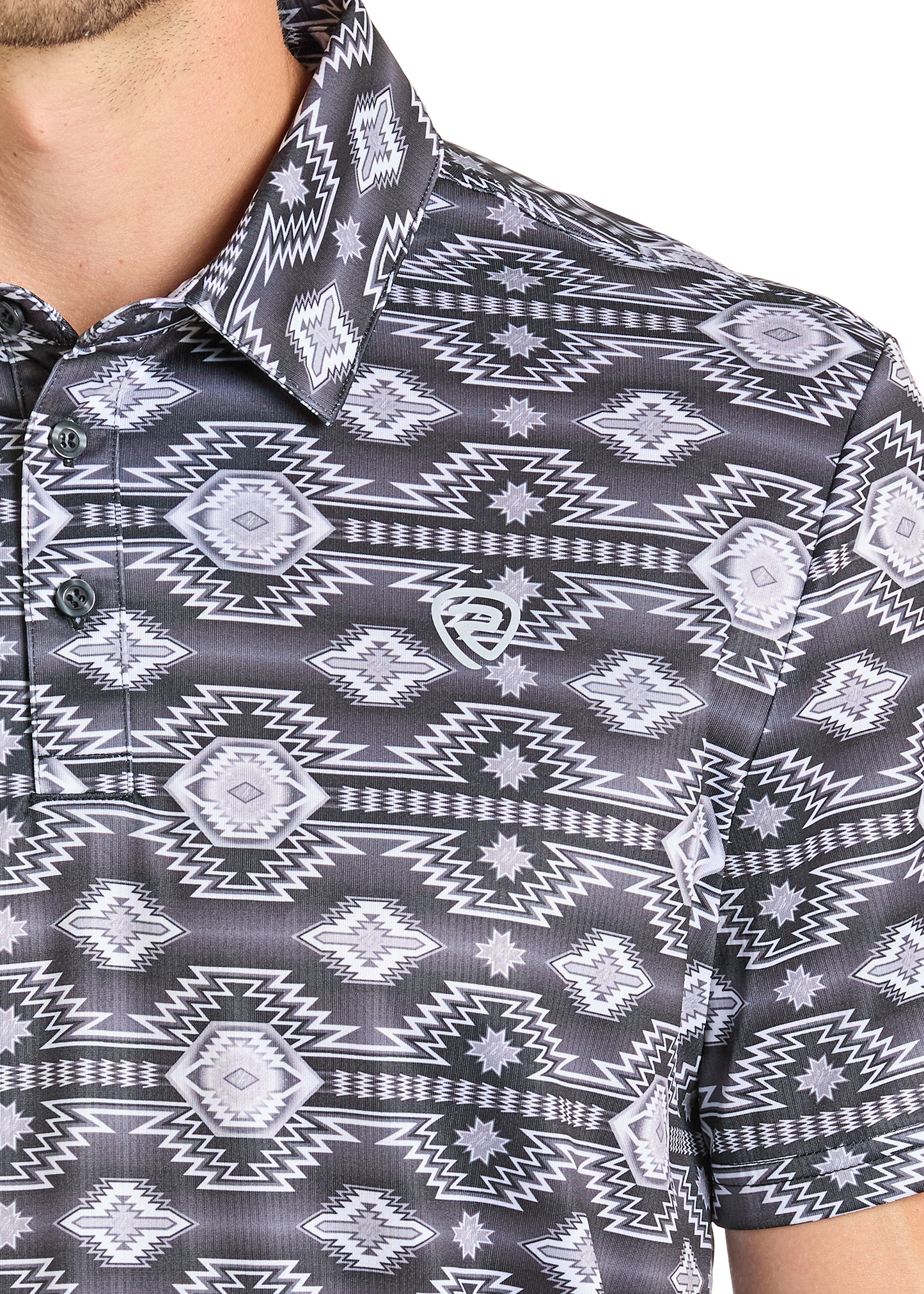 A close-up shows someone in the Rock & Roll Denim Black Traditional Aztec Polo, featuring a black and white geometric pattern, button-up style, small chest logo, and comfortable fit. Only part of their face and shoulder are visible.