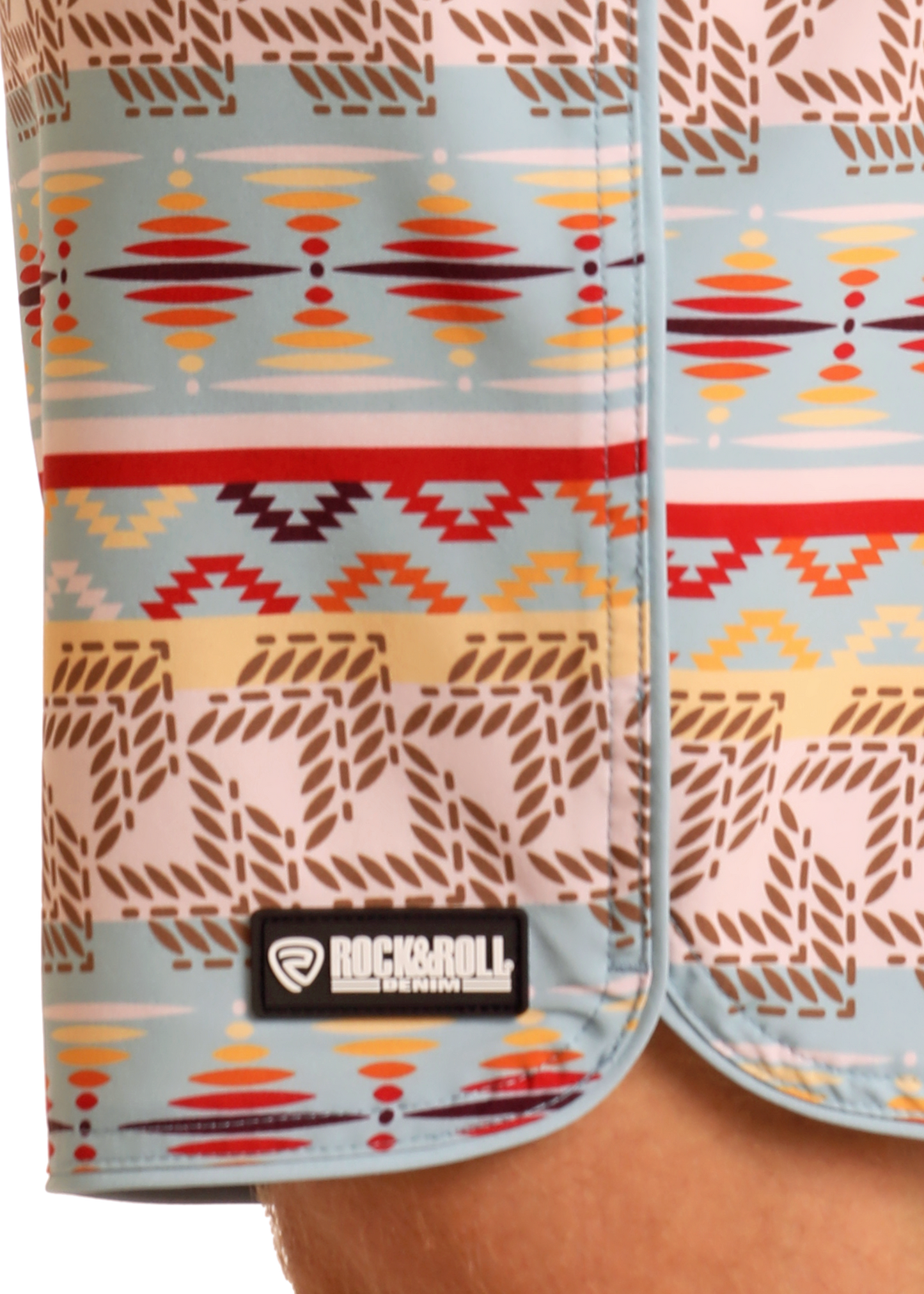 Close-up of Rock & Roll Denim Striped Aztec Board Shorts with a light blue base, colorful red, yellow, and brown geometric pattern, and a black-and-white brand label at the hem—ideal for stylish swimwear.