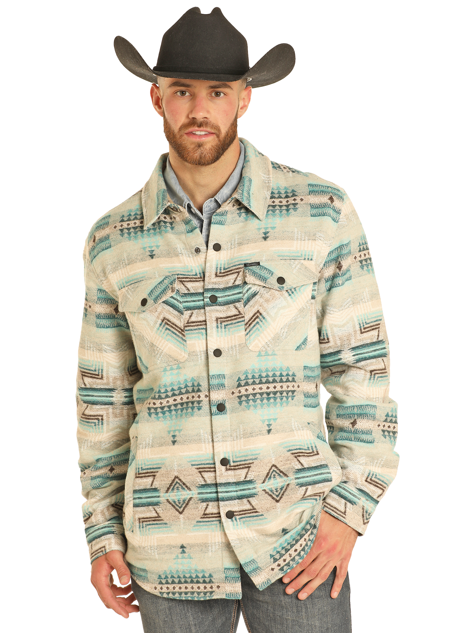 A man wearing a black cowboy hat, light blue shirt, gray jeans, and the Rock & Roll Denim Aztec Print Jacquard Shirt Jacket featuring cream, teal, beige, and black geometric designs stands facing forward with one hand in his pocket.