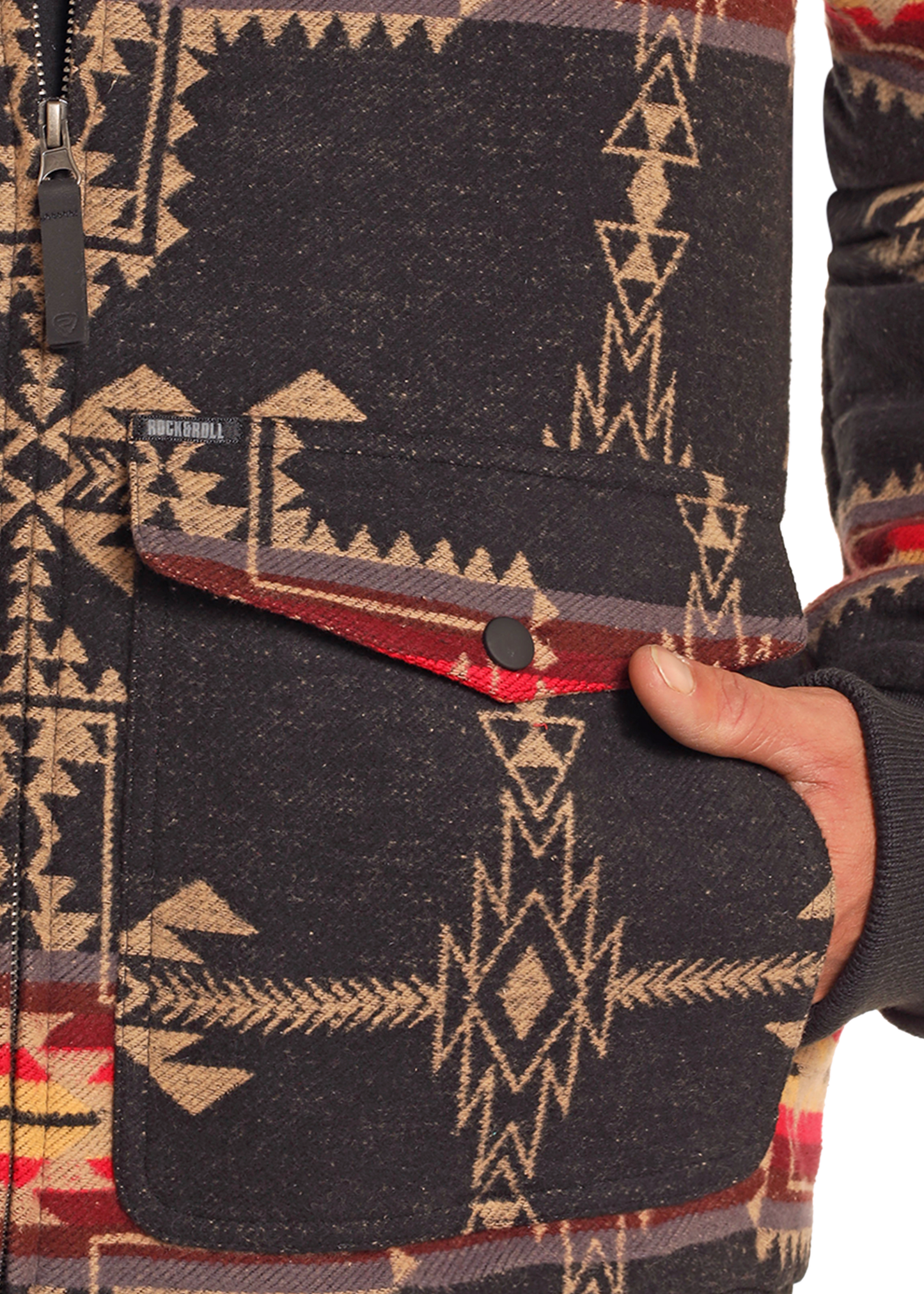 A close-up of a hand in the pocket of the Rock & Roll Denim Large Aztec Jacquard Bomber Jacket, featuring a bold geometric southwestern pattern in black, beige, and red, and a men's pocket with a stylish buttoned flap.