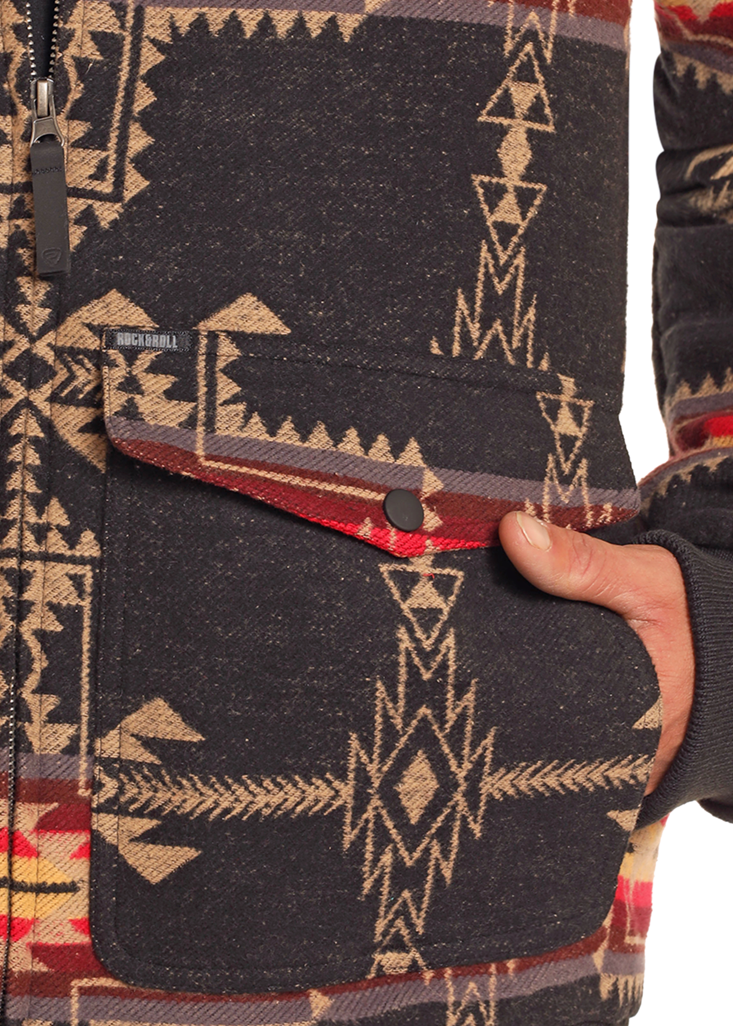 A close-up of a hand in the pocket of the Rock & Roll Denim Large Aztec Jacquard Bomber Jacket, featuring a bold geometric southwestern pattern in black, beige, and red, and a men's pocket with a stylish buttoned flap.