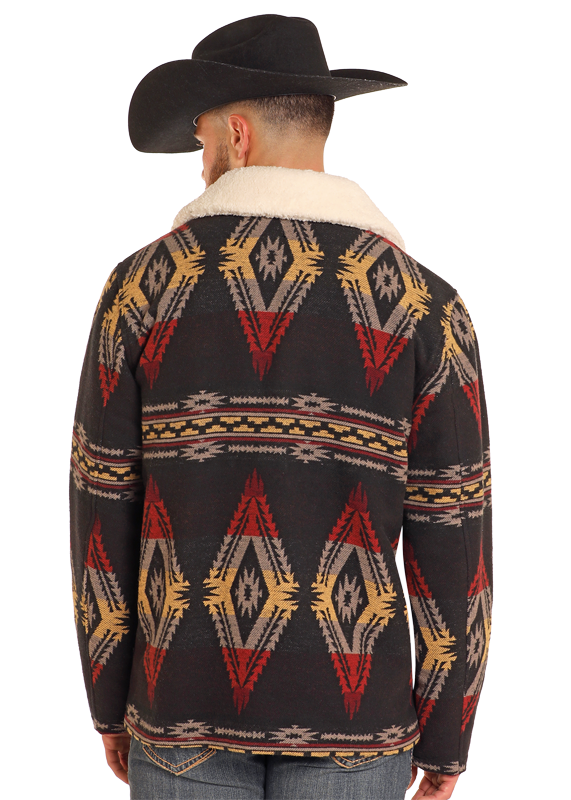 A man is shown from the back wearing a Rock & Roll Denim Black Aztec Jacquard Jacket featuring red, yellow, and beige geometric designs, a light-colored collar, a black cowboy hat, and classic blue jeans.