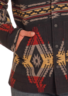 A person wearing the Rock & Roll Denim Black Aztec Jacquard Jacket, featuring red, yellow, gray, and black geometric patterns, has one hand in a side pocket; only the torso and part of an arm are visible.