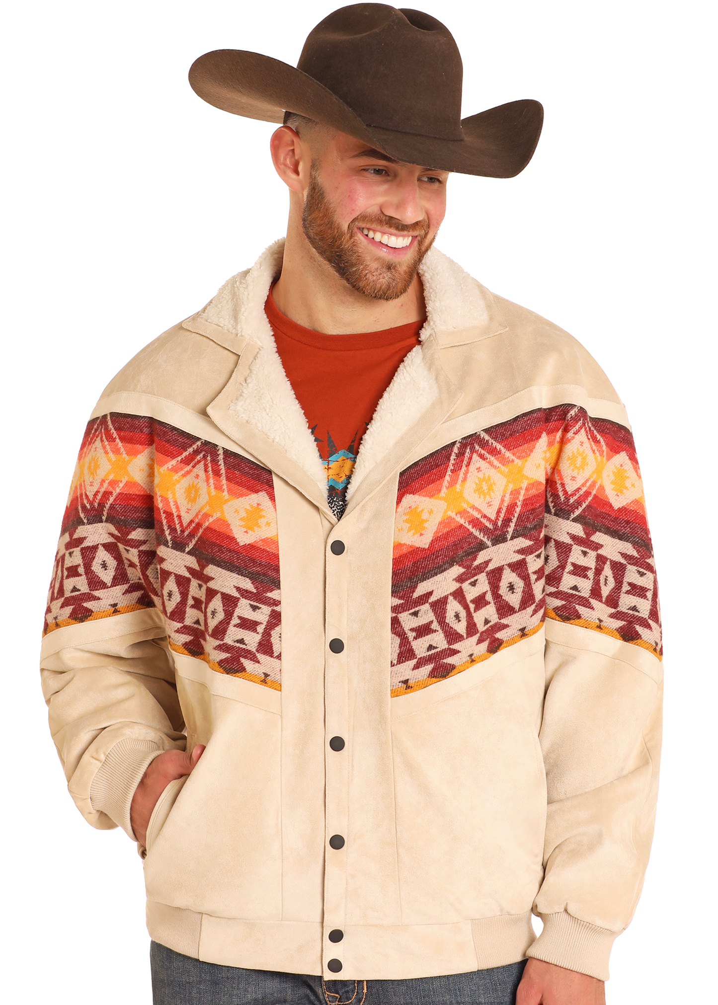 A smiling man in a Rock & Roll Denim Aztec Border Print Jacquard Jacket with a shearling collar, brown cowboy hat, orange shirt, and jeans stands with his hands in his pockets.