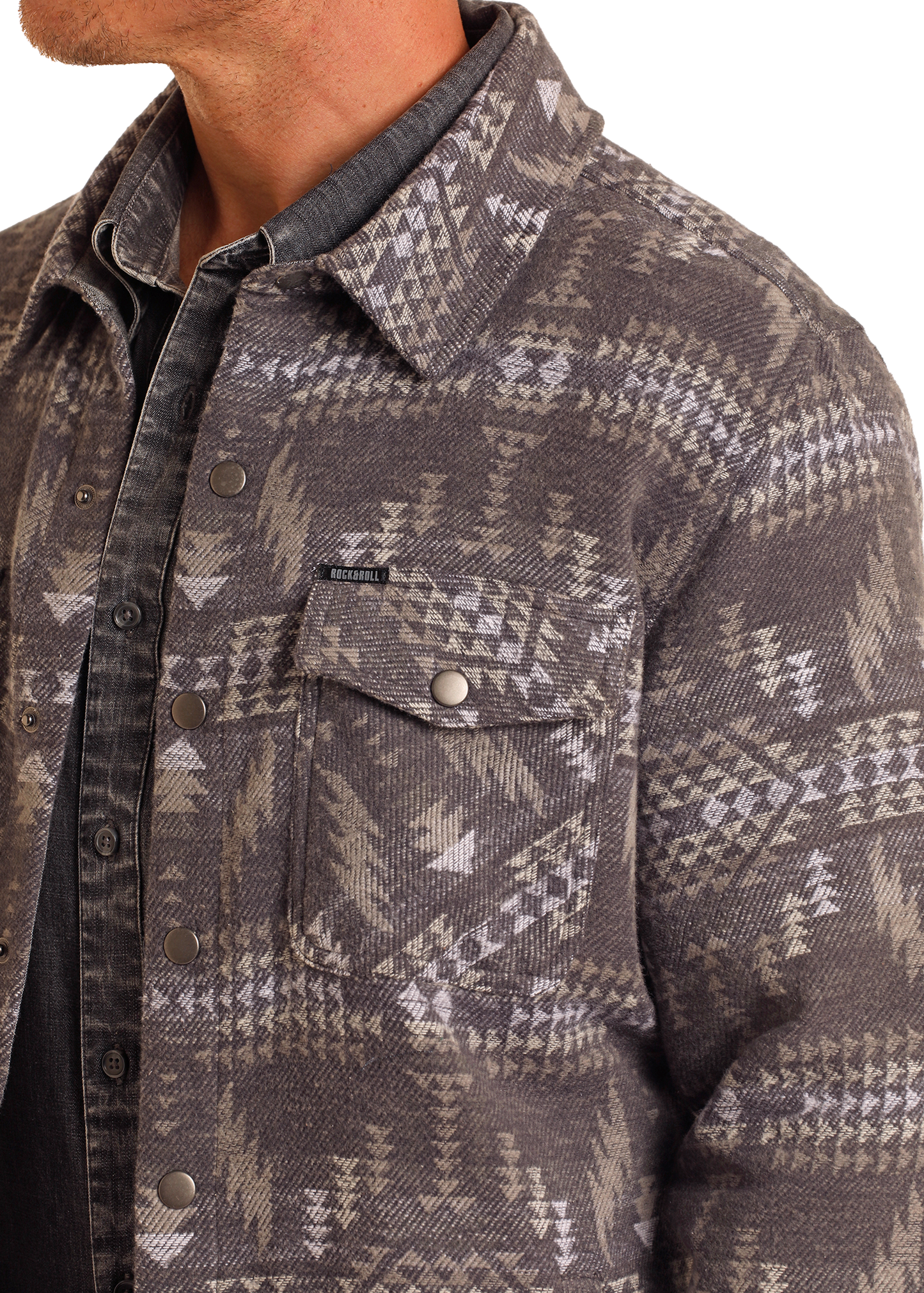 A person wears the Rock & Roll Denim Charcoal Aztec Jacquard Shirt Jacket, a patterned button-up with a flap chest pocket, in gray and beige tones over a dark shirt. Only the lower face, neck, and upper torso are visible.