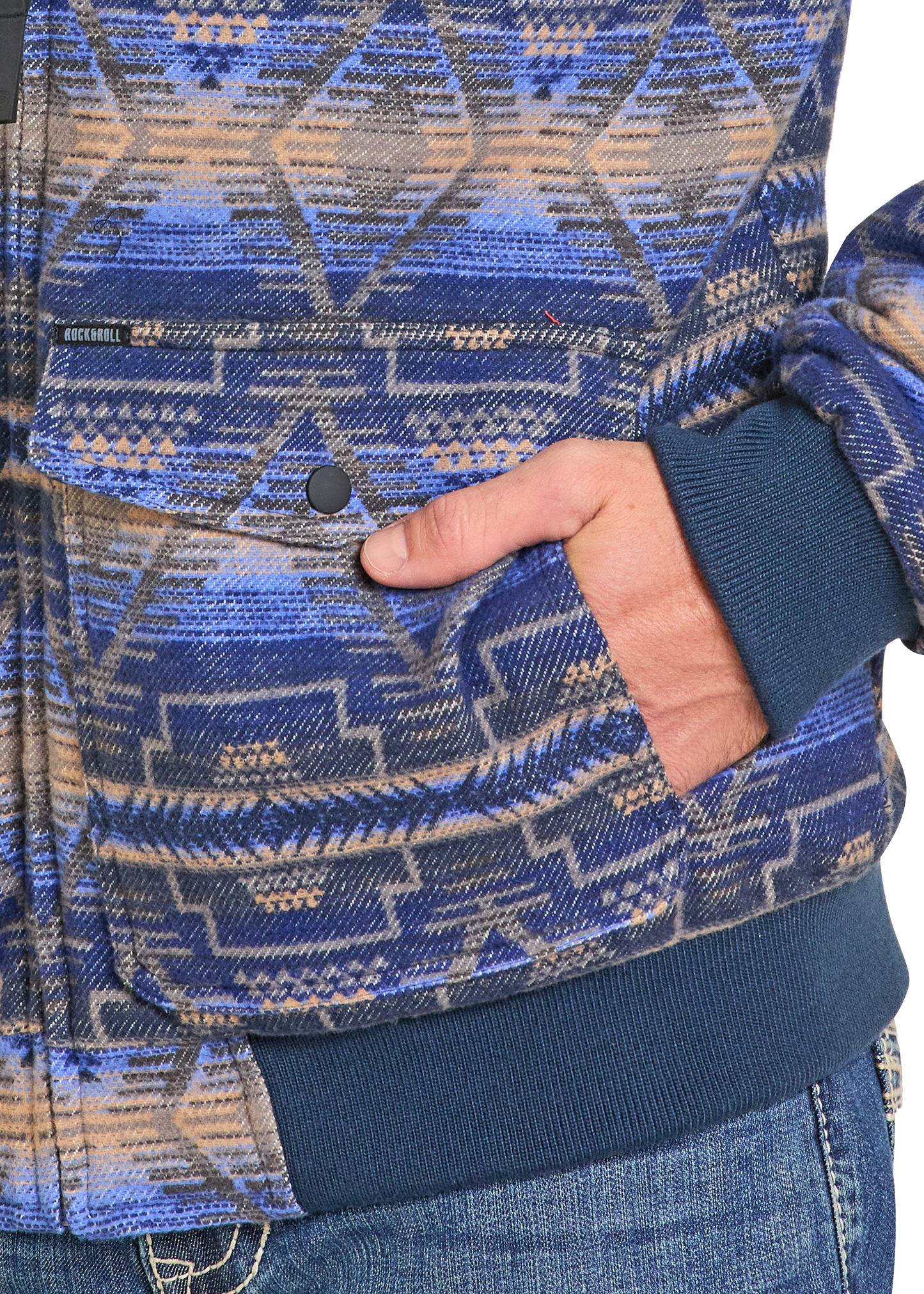 Close-up of a person wearing blue jeans and the Rock & Roll Denim Blue Aztec Jacquard Bomber Jacket, featuring geometric blue, beige, and gray patterns, with their right hand tucked into the pocket.