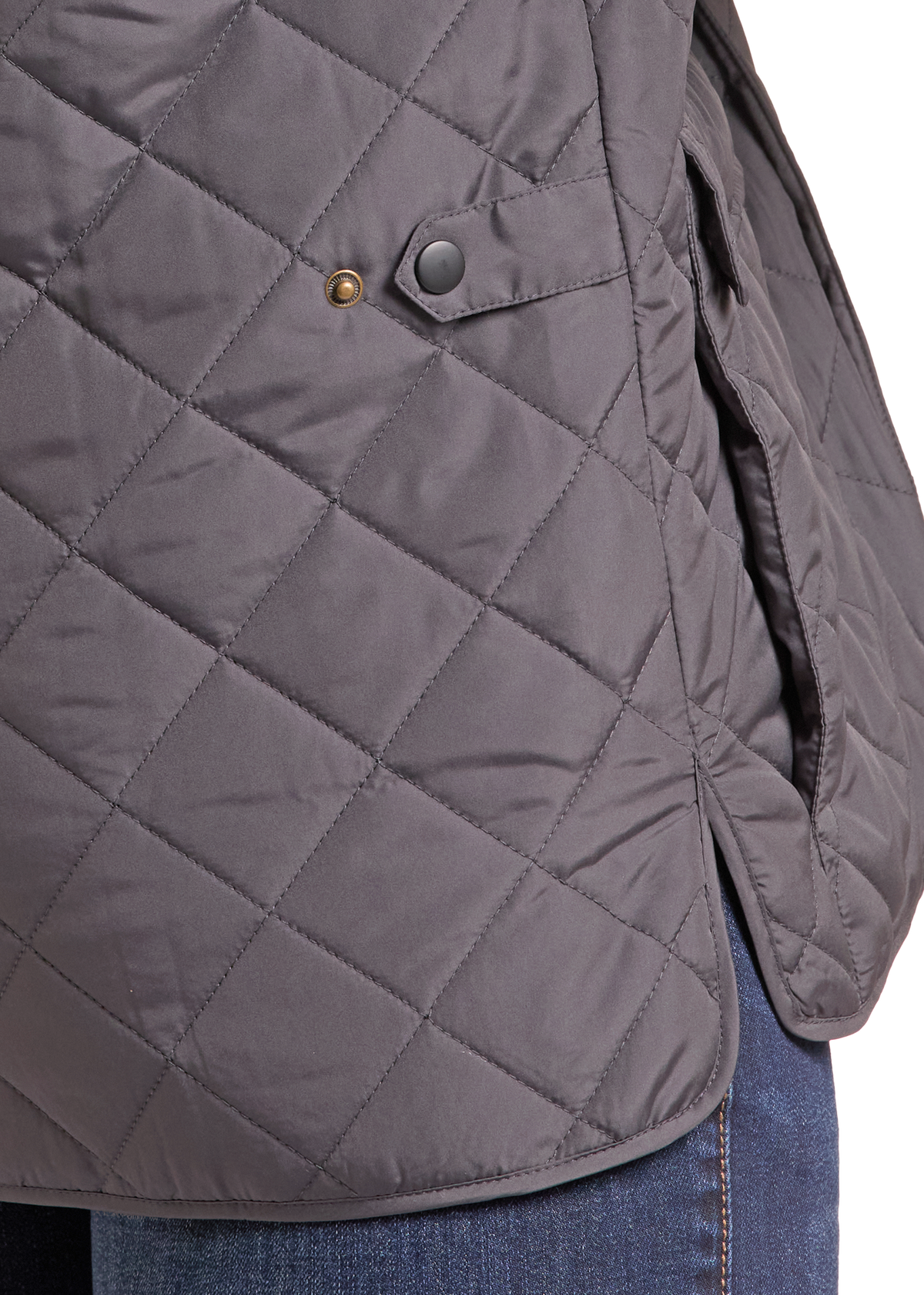 Close-up of a dark gray diamond-quilted puffer jacket with a snap-button flap detail, shown worn over blue jeans against a white background.