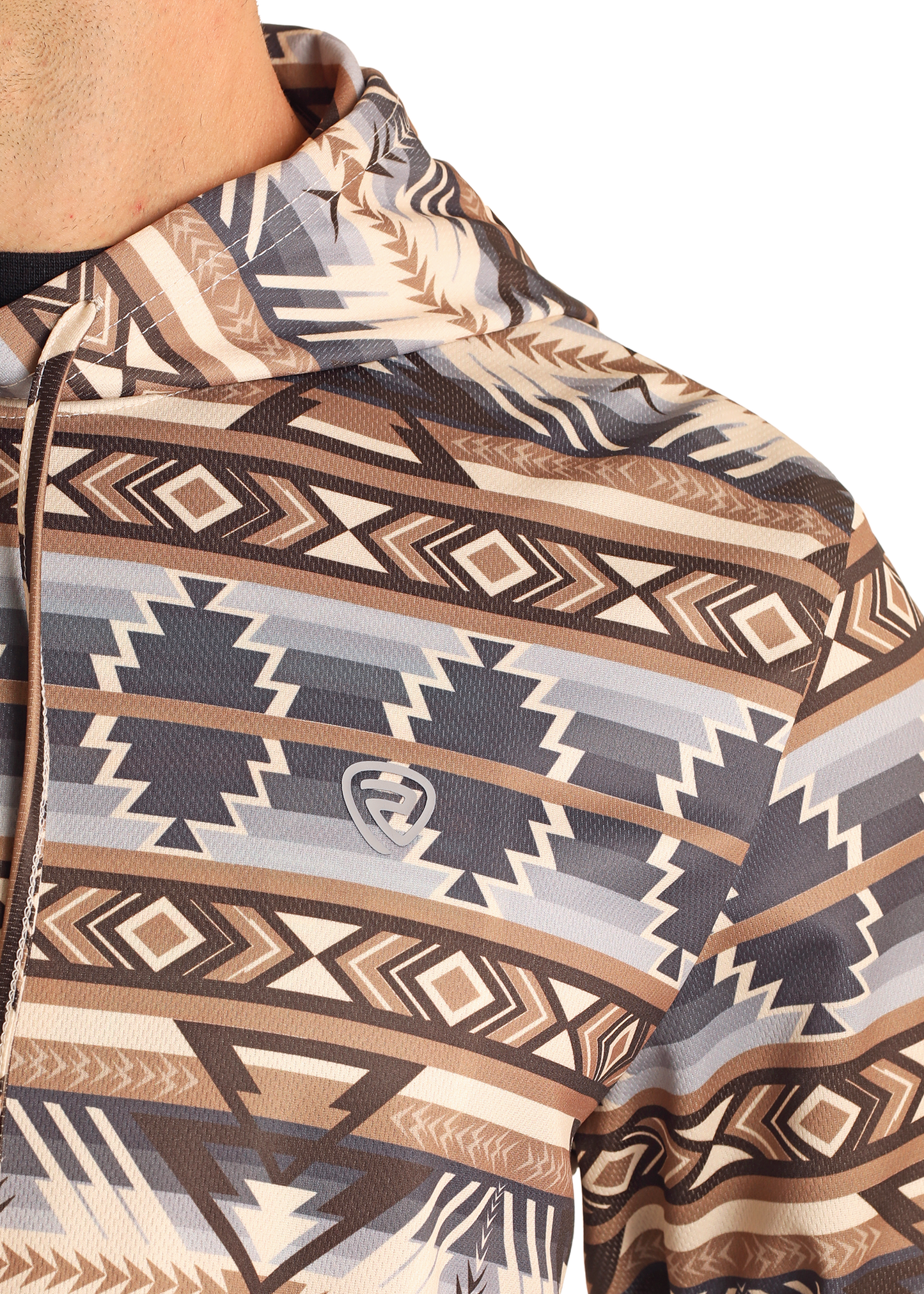 A close-up of someone wearing the Rock & Roll Denim Tan Aztec Performance Hoodie, featuring a geometric southwestern print in brown, tan, and gray with a small gray shield-shaped logo on the chest.
