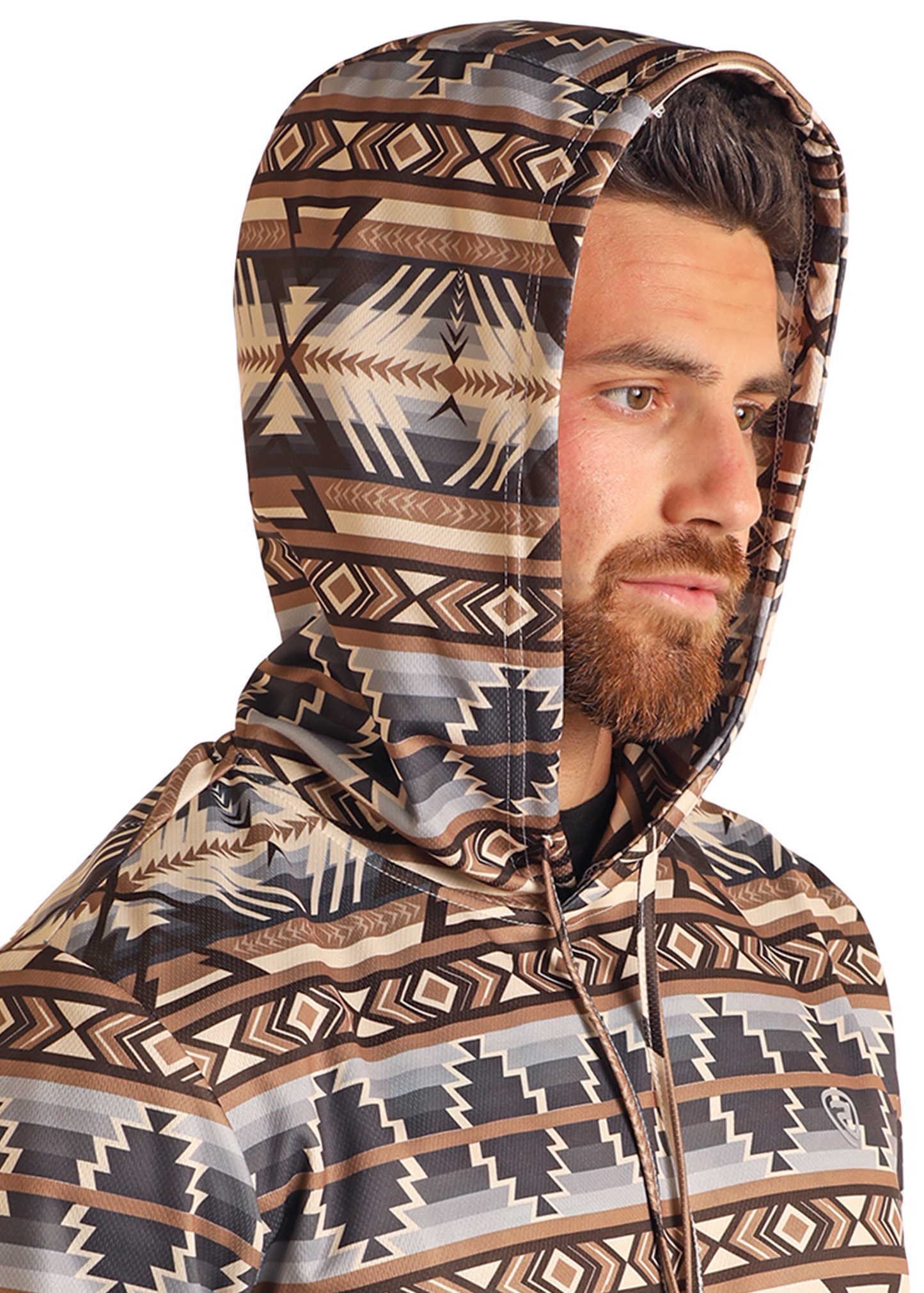 A bearded man wears the Rock & Roll Denim Tan Aztec Performance Hoodie, featuring a geometric tribal pattern in brown, beige, and black, as he looks off to the side against a plain background.