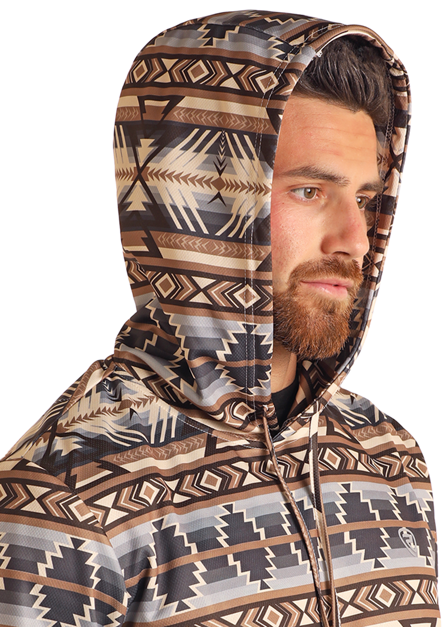 A bearded man wears the Rock & Roll Denim Tan Aztec Performance Hoodie, featuring a geometric tribal pattern in brown, beige, and black, as he looks off to the side against a plain background.