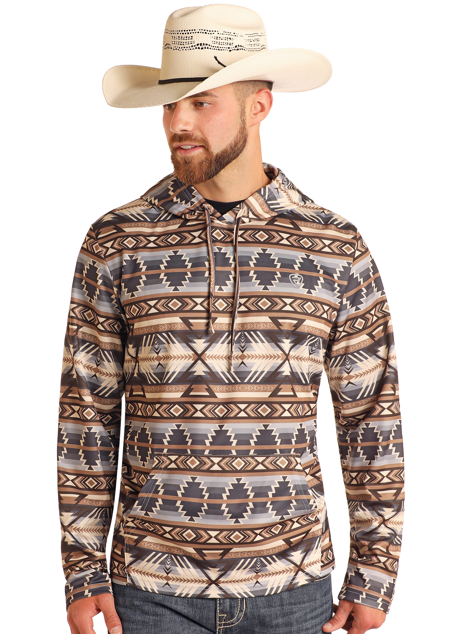 A man in the Rock & Roll Denim Tan Aztec Performance Hoodie, featuring earth-tone geometric designs, stands slightly to the side wearing a cream cowboy hat, jeans, and sporting a trimmed beard.
