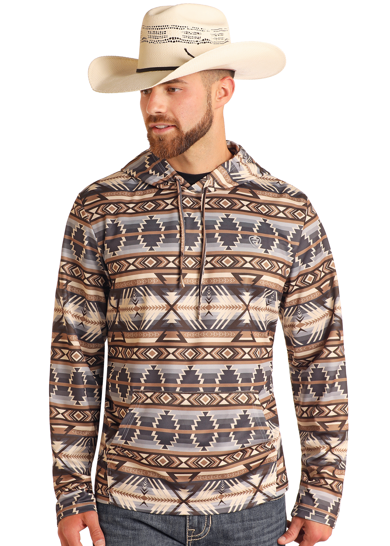 A man in the Rock & Roll Denim Tan Aztec Performance Hoodie, featuring earth-tone geometric designs, stands slightly to the side wearing a cream cowboy hat, jeans, and sporting a trimmed beard.