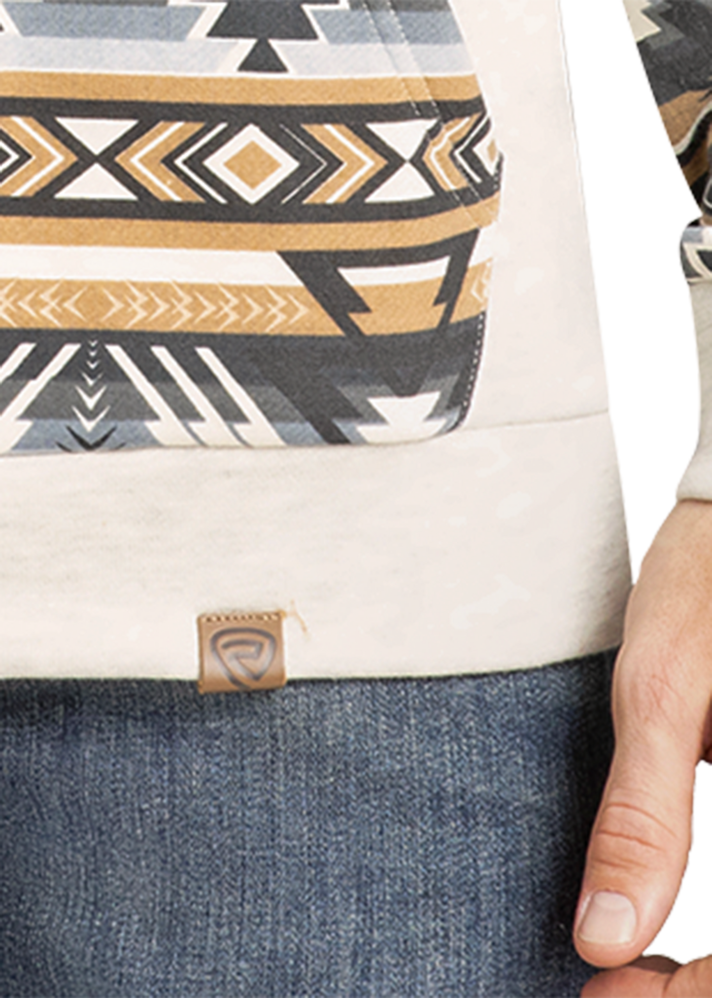 A person wears blue jeans and Rock & Roll Denim’s Aztec Accented Hoodie in cream, with a geometric tribal pattern in gold, black, and gray. Only the lower torso and right hand are visible.