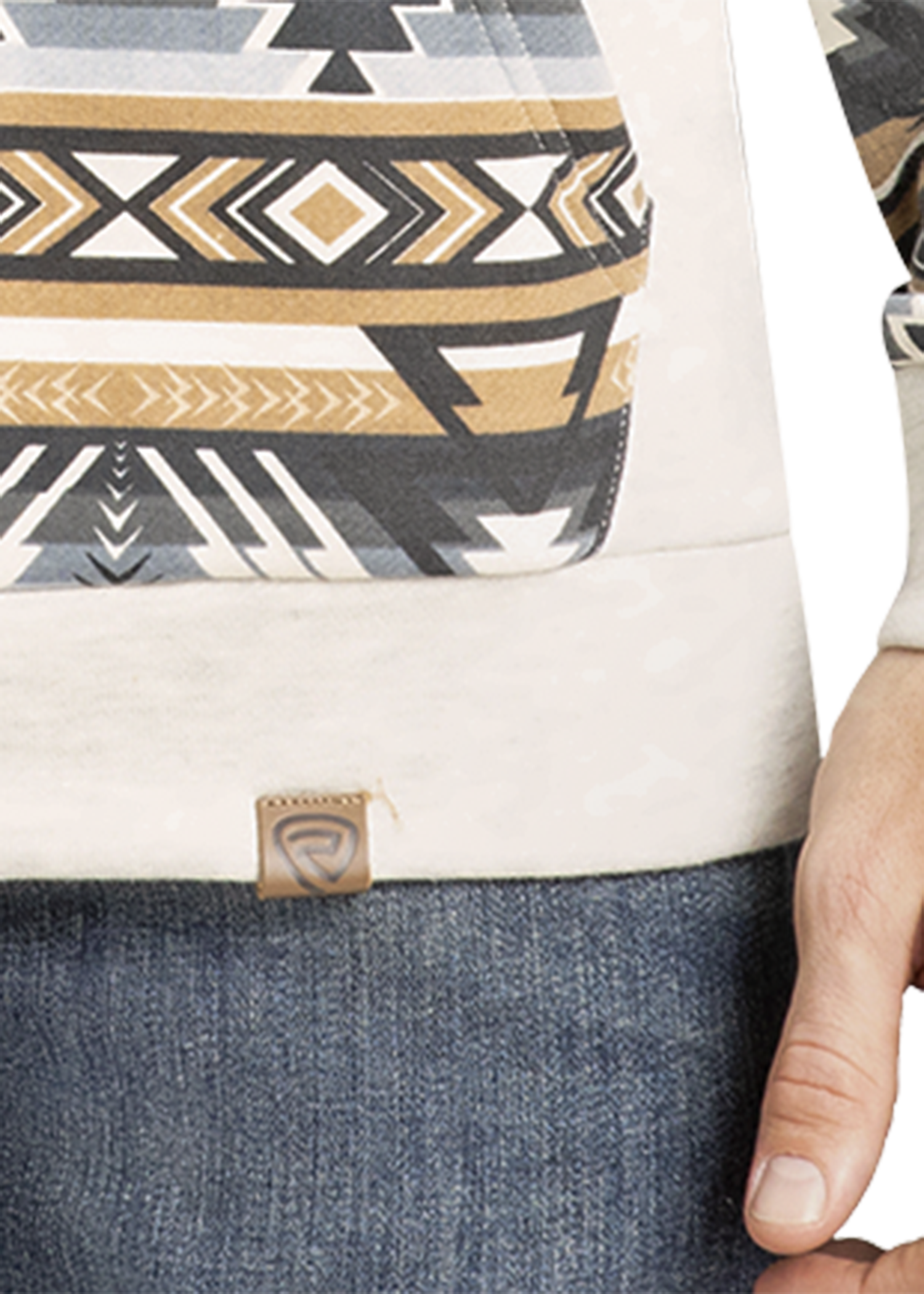 A person wears blue jeans and Rock & Roll Denim’s Aztec Accented Hoodie in cream, with a geometric tribal pattern in gold, black, and gray. Only the lower torso and right hand are visible.