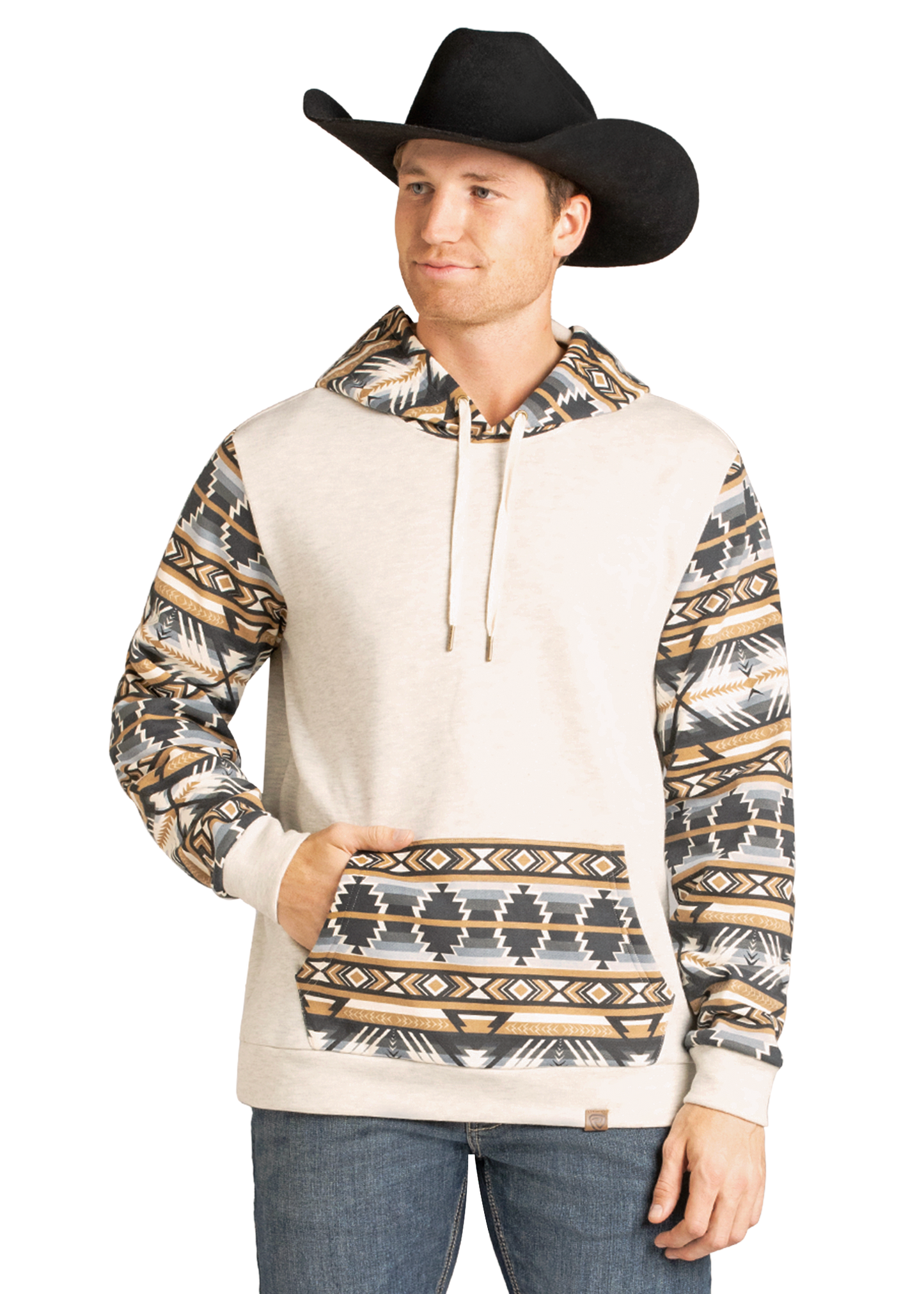A man wearing a black cowboy hat, blue jeans, and the Rock & Roll Denim Aztec Accented Hoodie with southwest-style patterned sleeves, hood, and pocket stands with one hand in his hoodie pocket and smiles slightly.