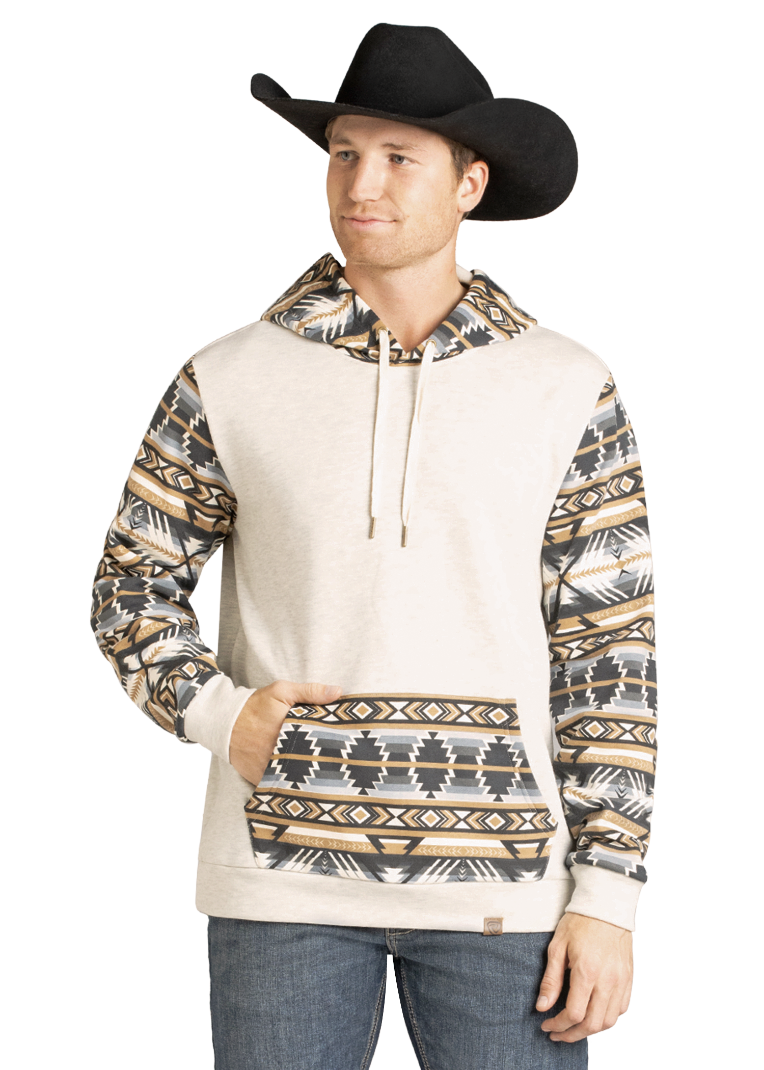 A man wearing a black cowboy hat, blue jeans, and the Rock & Roll Denim Aztec Accented Hoodie with southwest-style patterned sleeves, hood, and pocket stands with one hand in his hoodie pocket and smiles slightly.