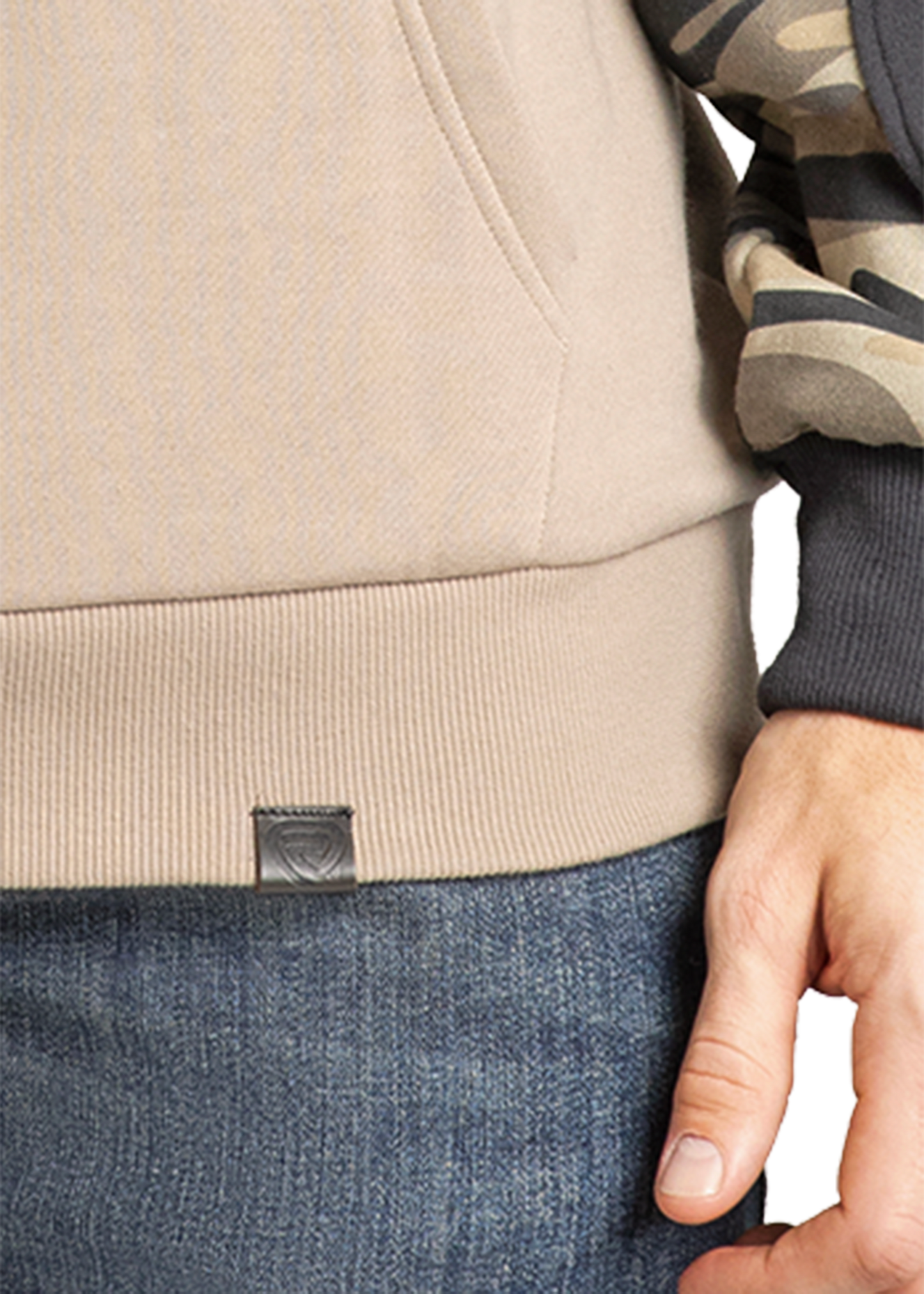 A close-up of a person’s hand by their side, wearing blue jeans and the Rock & Roll Denim Camo Block Hoodie—a beige hoodie with a camouflage sleeve and signature kangaroo pocket.