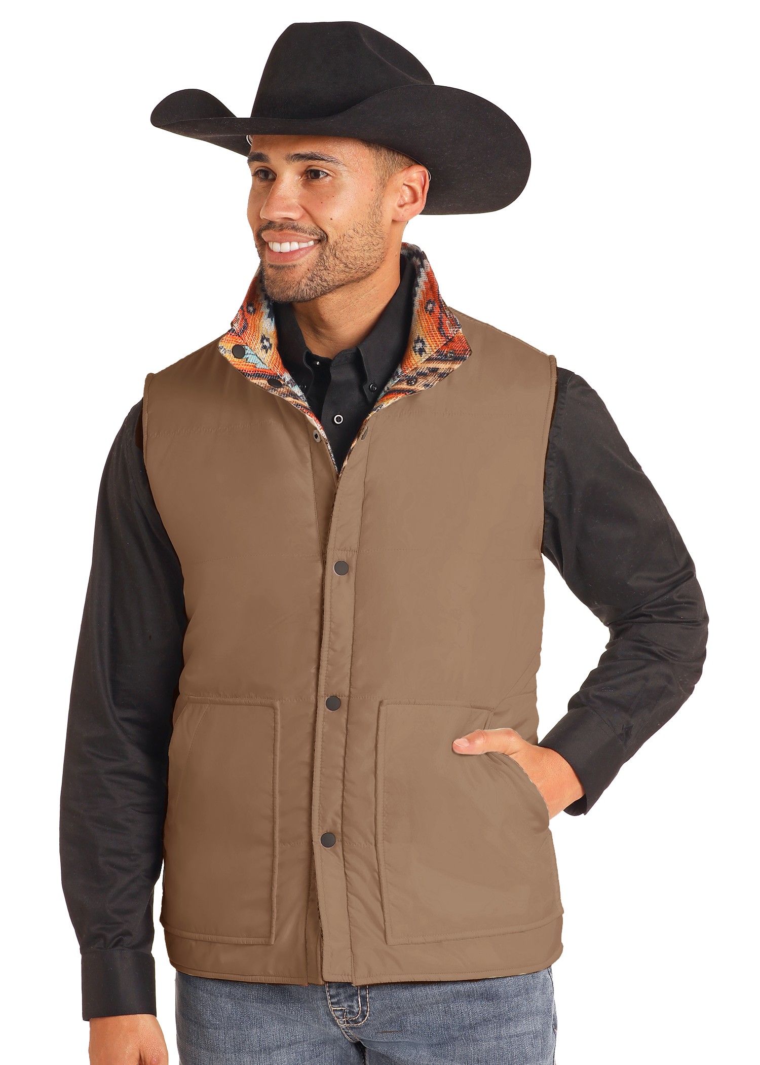 A smiling man stands with one hand in his pocket, wearing a black cowboy hat, a black shirt, and the Reversible Aztec Jacquard Vest by Rock & Roll Denim, effortlessly highlighting classic men's style against a plain background.