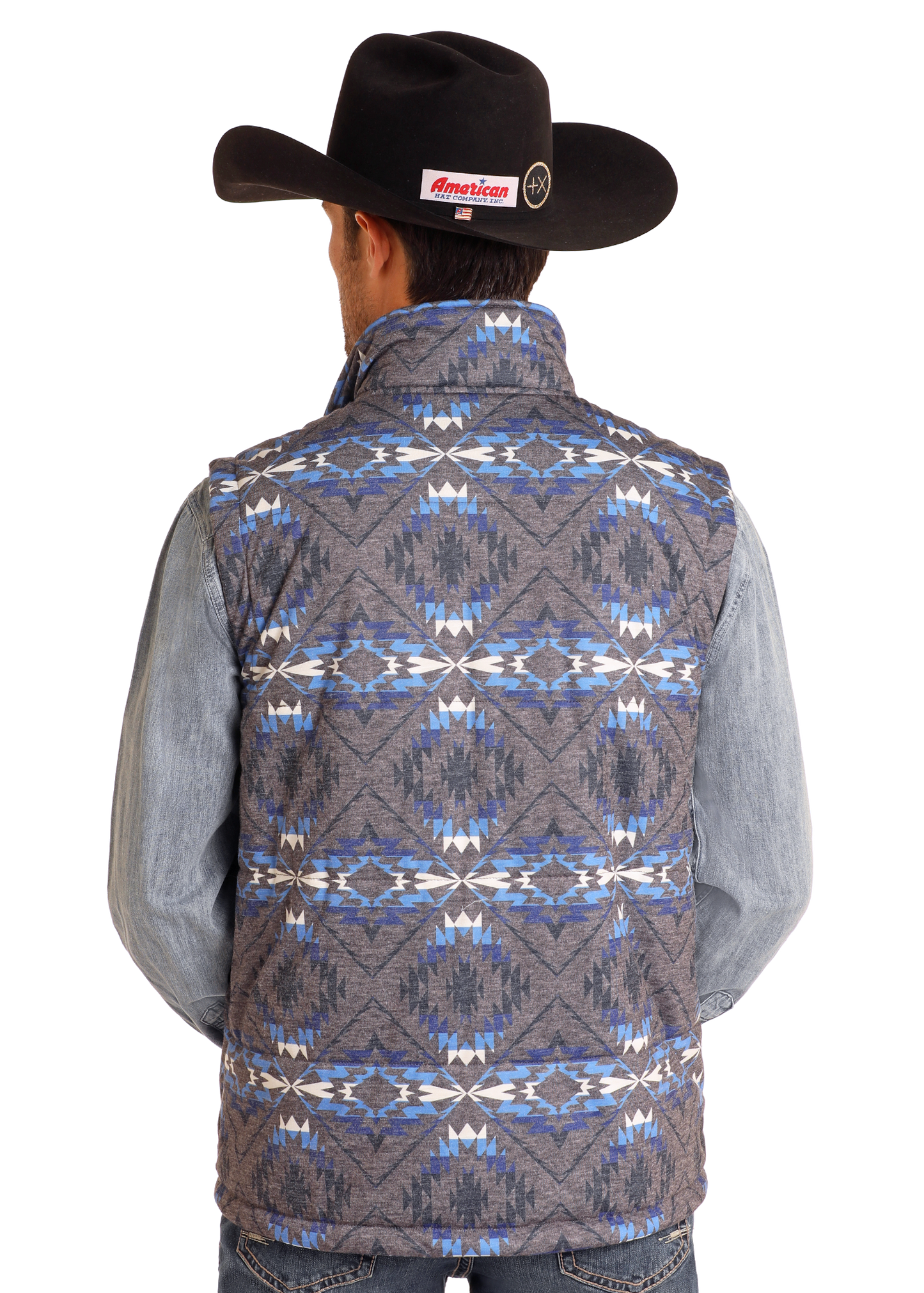 A man wearing a black cowboy hat, a gray long-sleeve shirt, and the Rock & Roll Denim Aztec Print Puffer Vest with blue, white, and gray geometric patterns stands facing away from the camera.