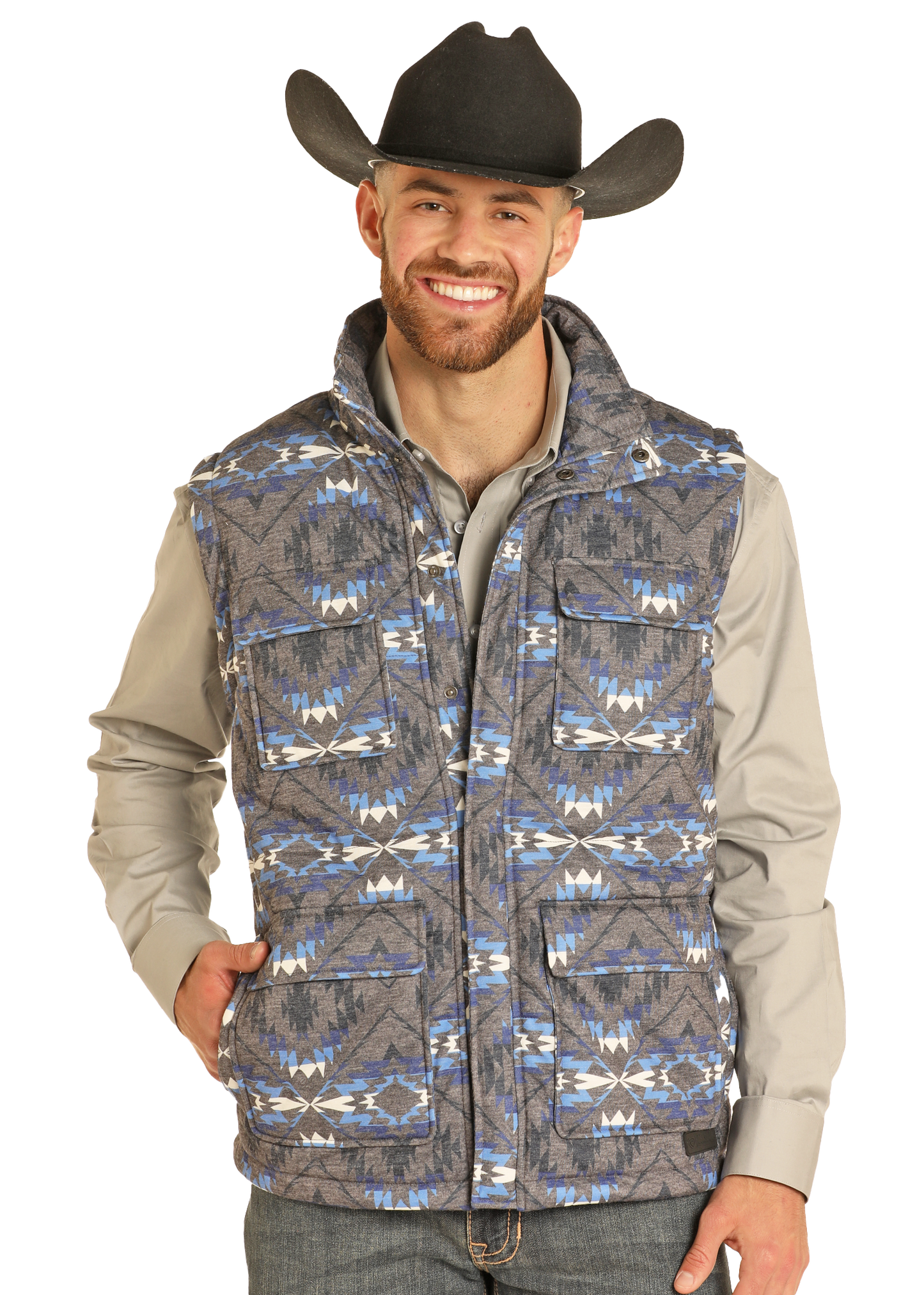 A smiling man in a black cowboy hat wears a gray button-up shirt and the Rock & Roll Denim Aztec Print Puffer Vest, featuring bold geometric designs, as he stands with one hand in his pocket against a plain background.