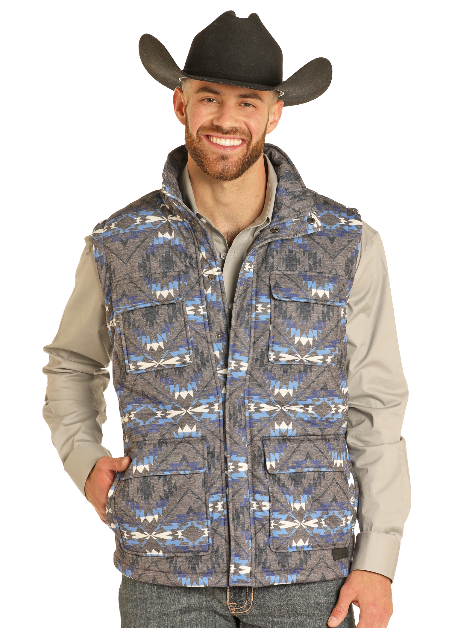A smiling man in a black cowboy hat wears a gray button-up shirt and the Rock & Roll Denim Aztec Print Puffer Vest, featuring bold geometric designs, as he stands with one hand in his pocket against a plain background.