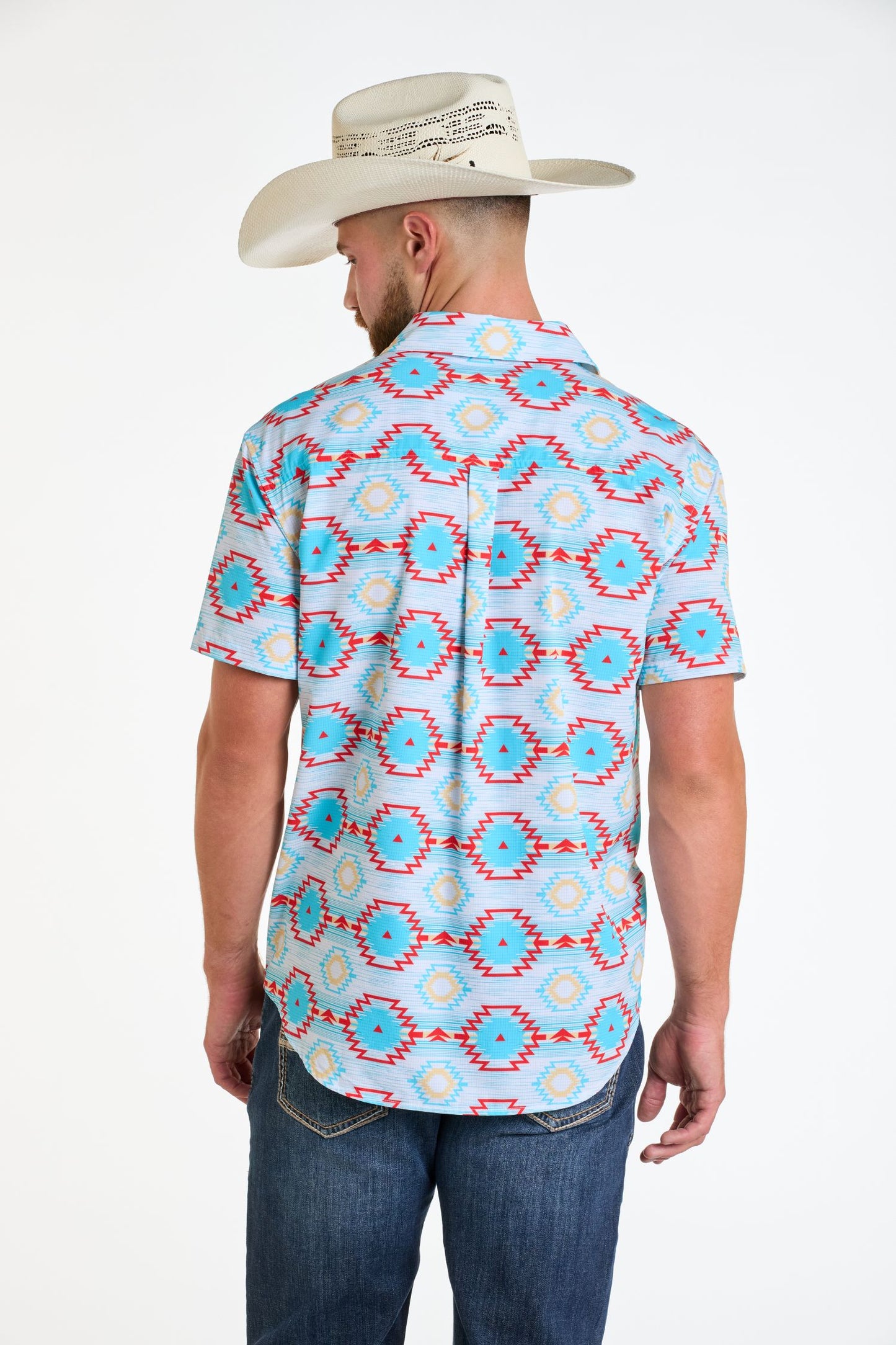 A man in a white cowboy hat, blue jeans, and a Rock & Roll Denim TEK Western Aztec Button Short Sleeve Shirt with red and yellow geometric patterns stands facing away against a plain white background.