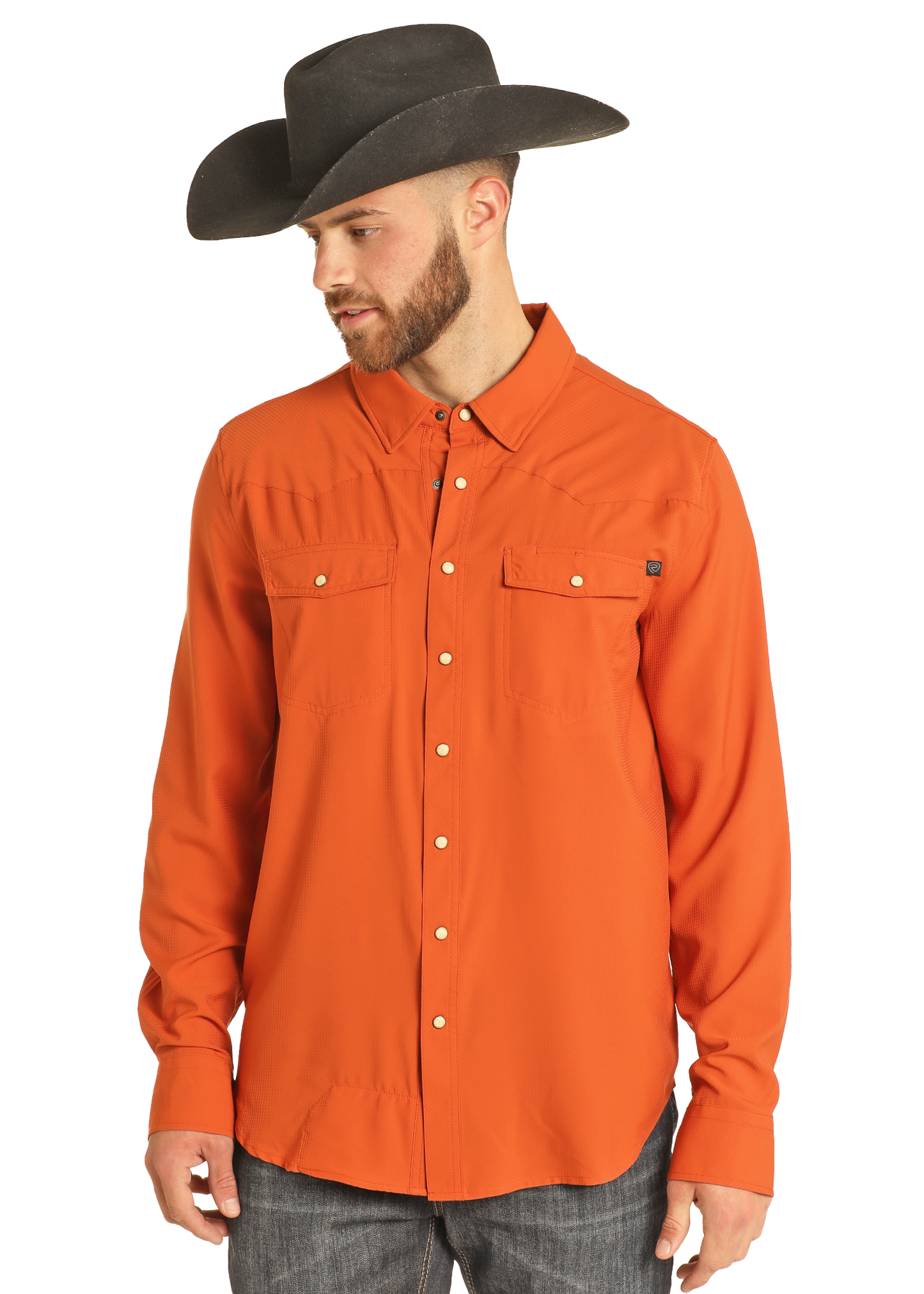 A man wears the Rock & Roll Denim TEK Western Burnt Orange Long Sleeve Shirt and a wide-brimmed black cowboy hat, looking down and to the side against a plain white background.