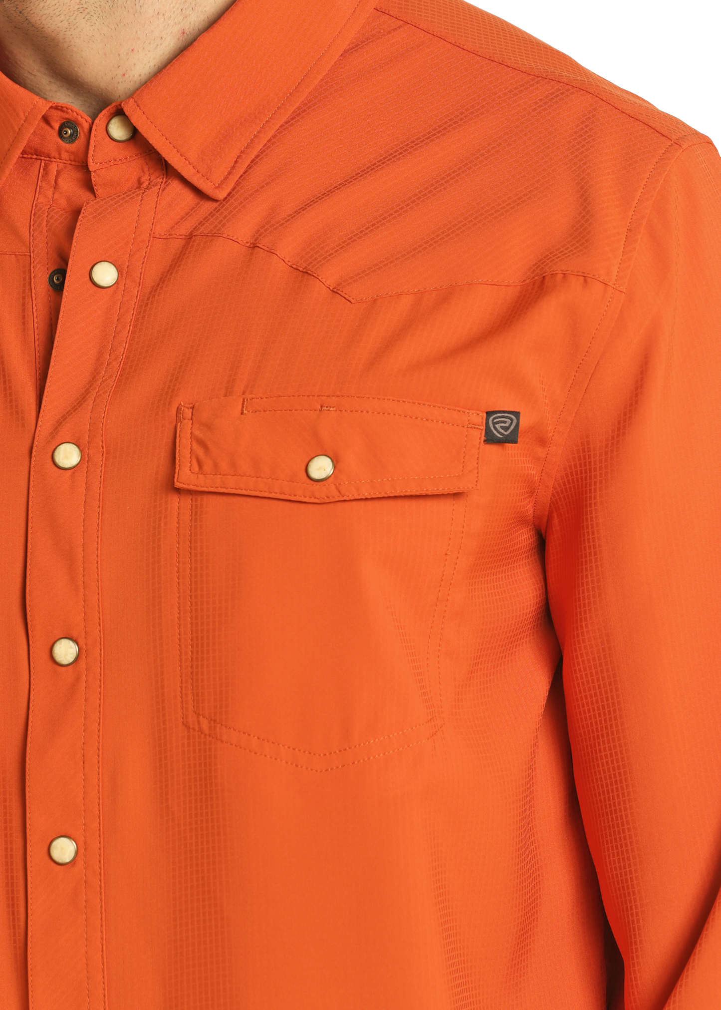 A close-up shows the upper torso of a person wearing the Rock & Roll Denim TEK Western Burnt Orange Long Sleeve Shirt, featuring a chest pocket with a small black tag and white snap buttons. Only part of the neck is visible.