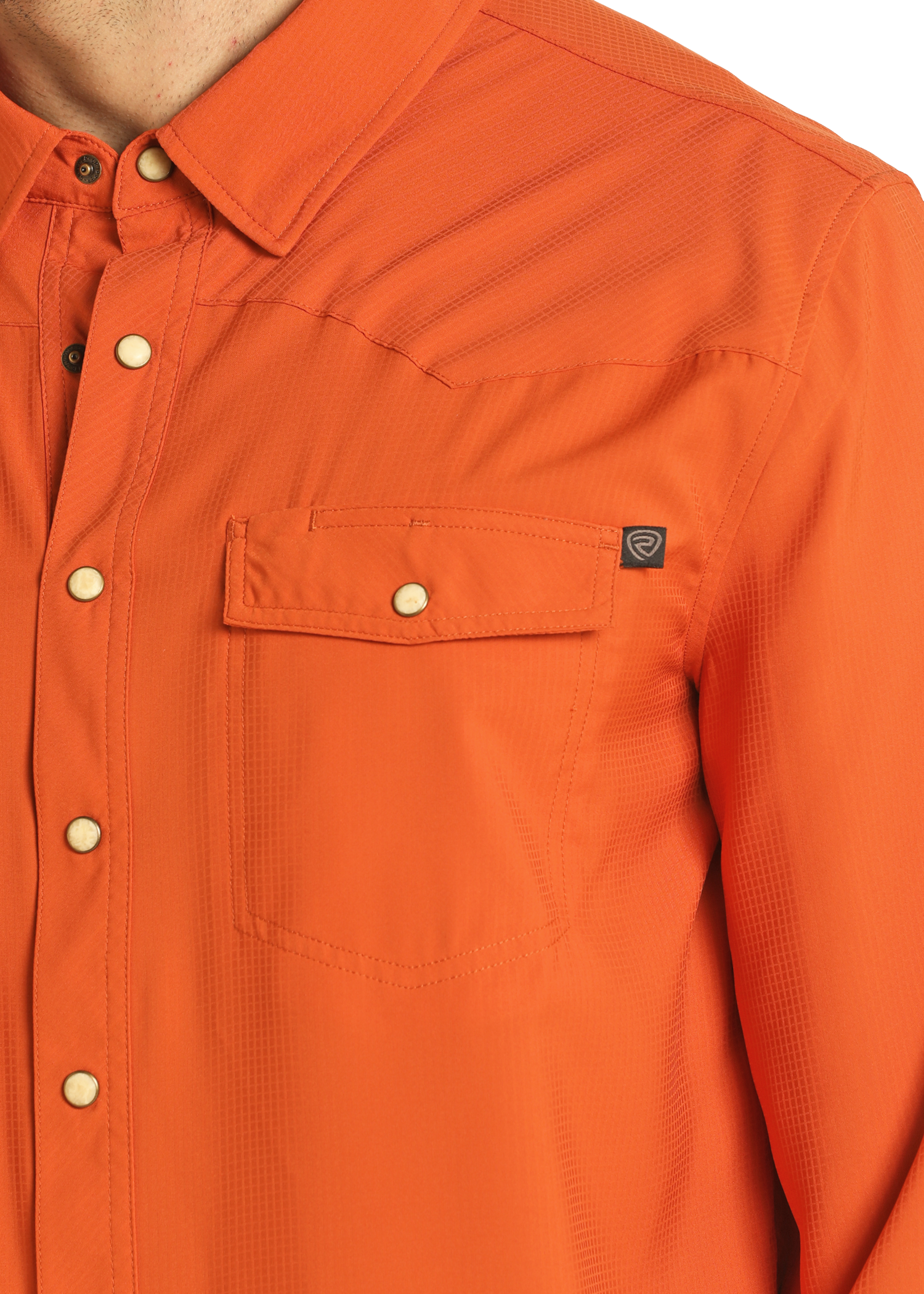 A close-up shows the upper torso of a person wearing the Rock & Roll Denim TEK Western Burnt Orange Long Sleeve Shirt, featuring a chest pocket with a small black tag and white snap buttons. Only part of the neck is visible.