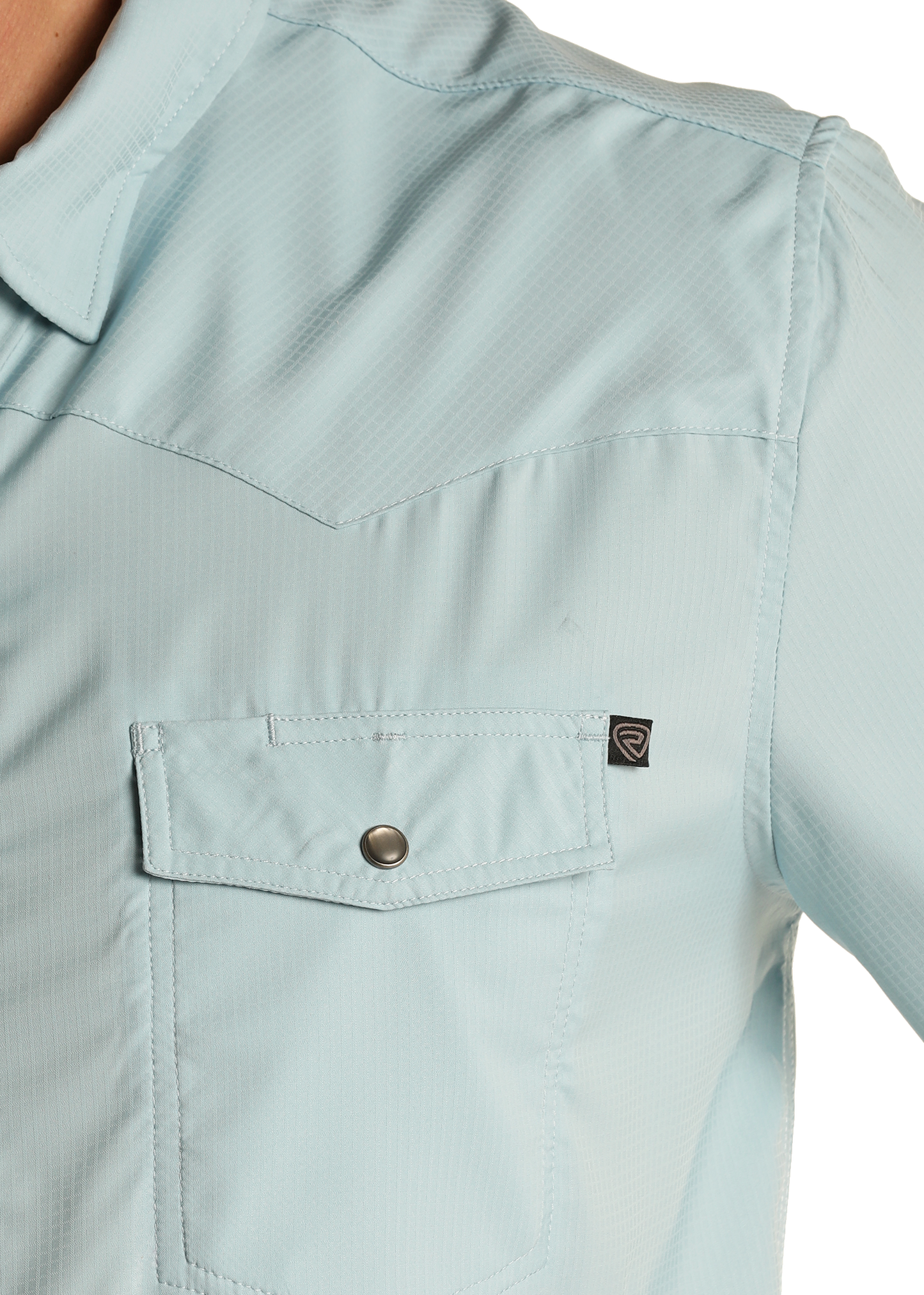 Close-up of the Rock & Roll Denim TEK Western Aqua Long Sleeve Shirt, featuring moisture-wicking light blue fabric, a chest pocket with flap and snap button, small black tag, and visible stitching details.
