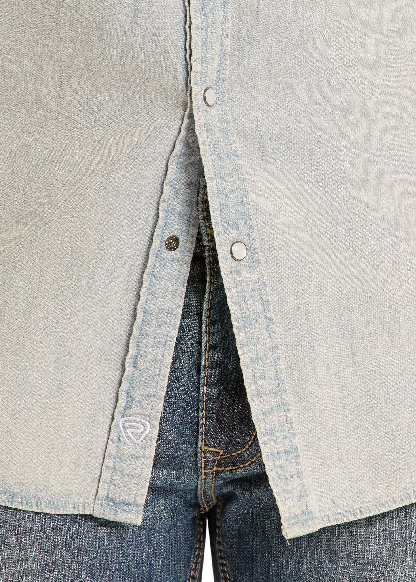 Close-up of the Rock & Roll Denim Slim Fit Light Wash Denim Snap Shirt, slightly open at the bottom to reveal blue jeans. Features snap buttons and a small white embroidered logo near the hem.