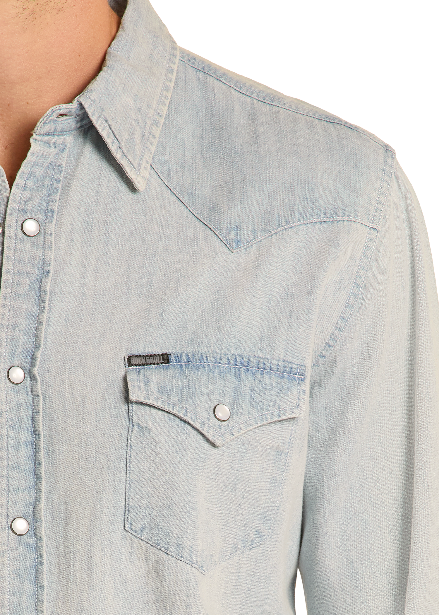Close-up of a person wearing the Rock & Roll Denim Slim Fit Light Wash Denim Snap Shirt, featuring metal snap buttons, a pointed collar, and a chest pocket with flap and button closure. Upper torso only is visible. The slim fit gives a modern look.