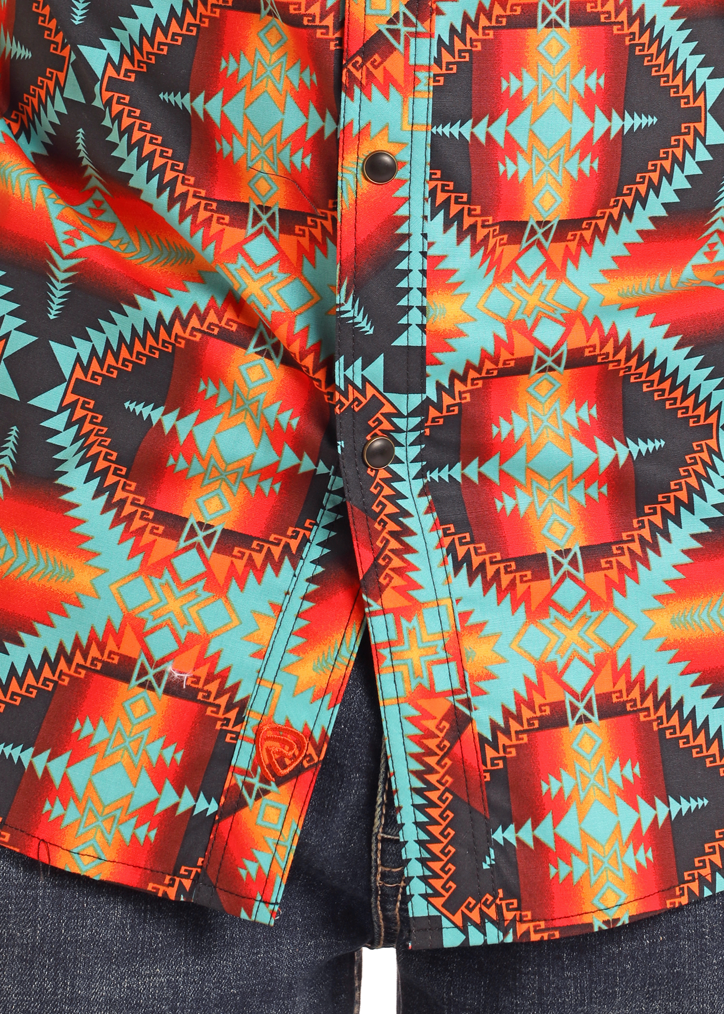 Close-up of the Rock & Roll Denim Slim Fit Red Aztec Long Sleeve Snap Shirt with a vibrant geometric pattern in red, orange, teal, and black, styled with dark blue denim jeans.