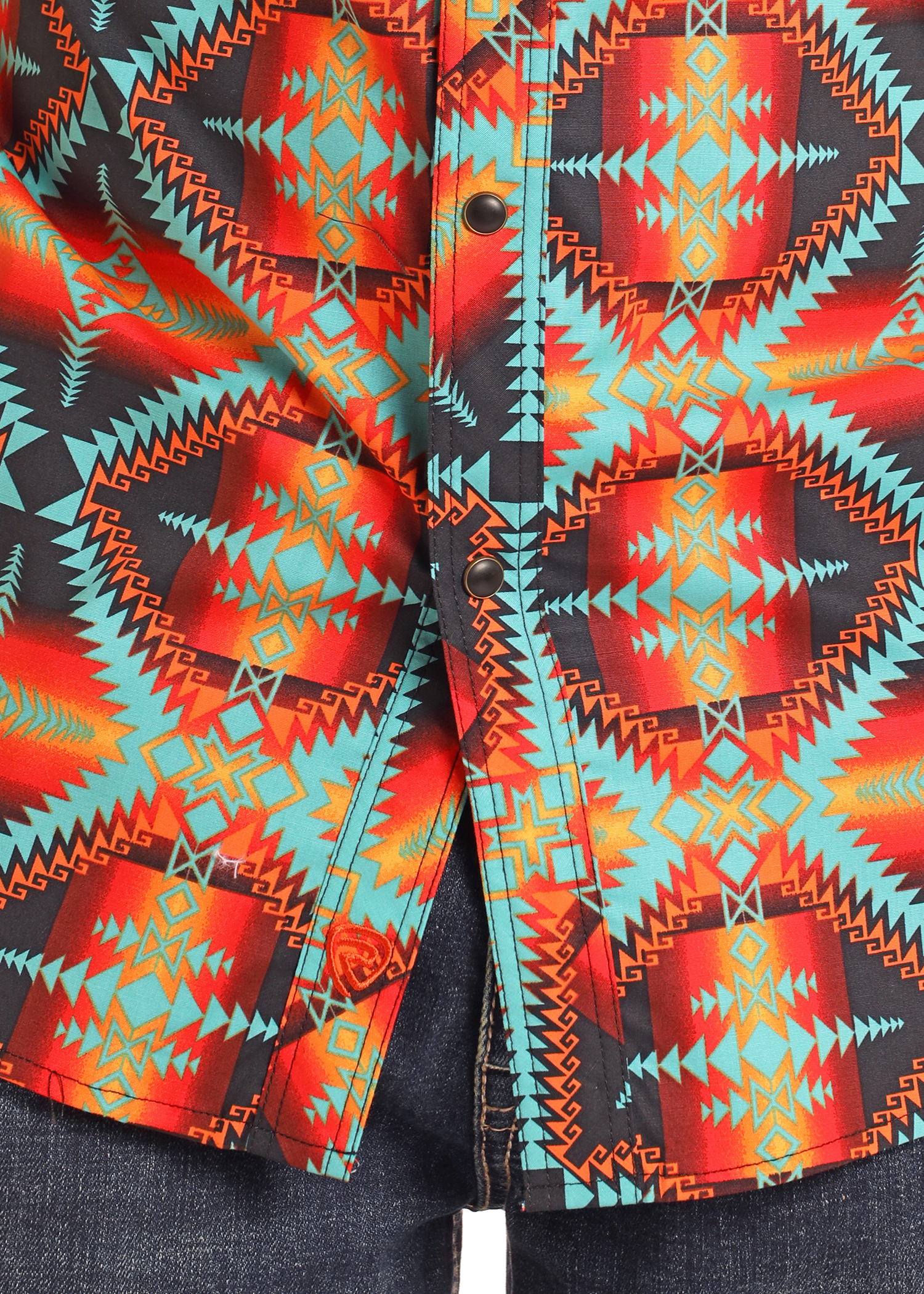 Close-up of the Rock & Roll Denim Slim Fit Red Aztec Long Sleeve Snap Shirt with a vibrant geometric pattern in red, orange, teal, and black, styled with dark blue denim jeans.