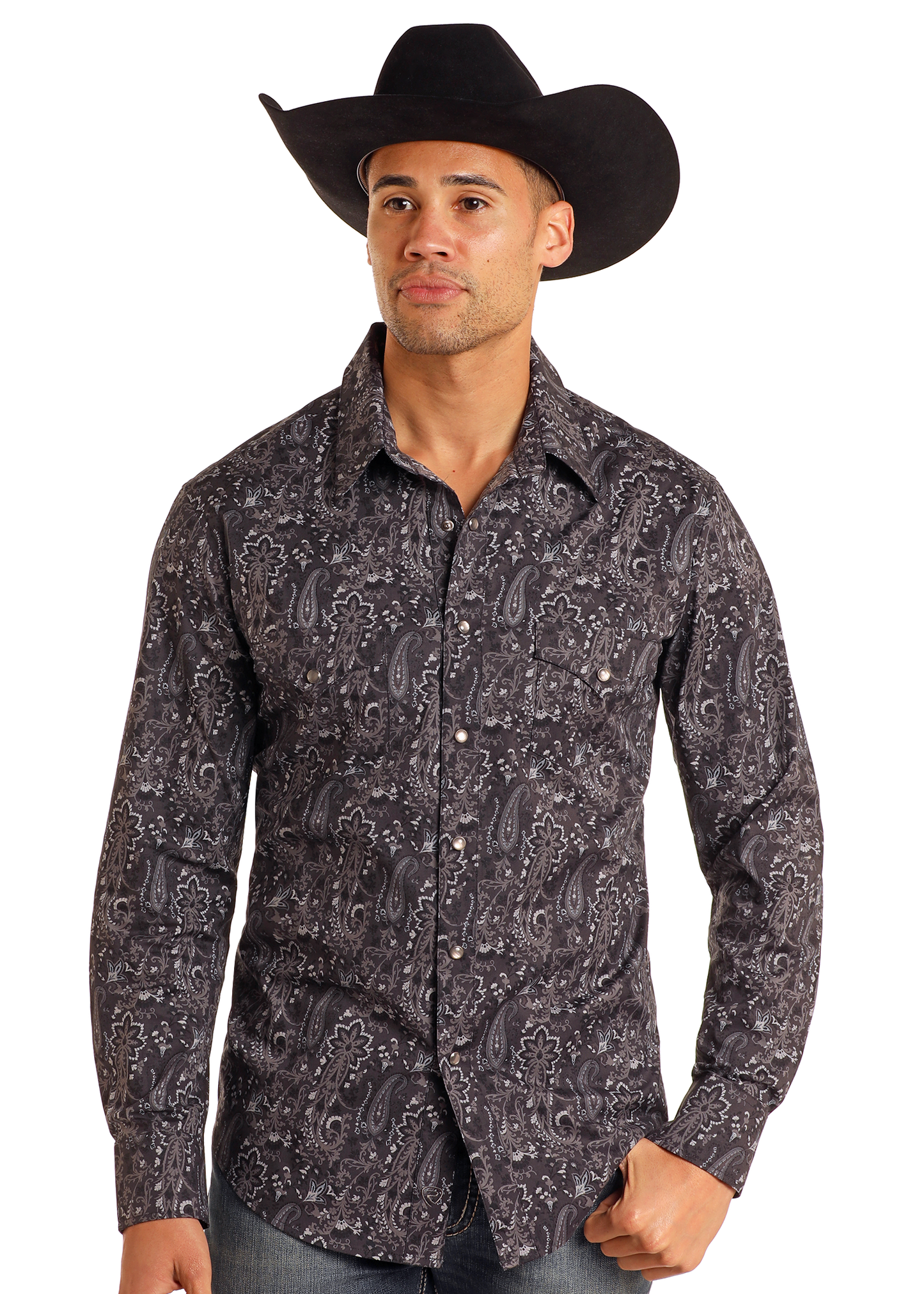 A man wearing a large black cowboy hat, blue jeans, and a Rock & Roll Denim Slim Fit Black Paisley Print Long Sleeve Snap Shirt stands against a plain white background.