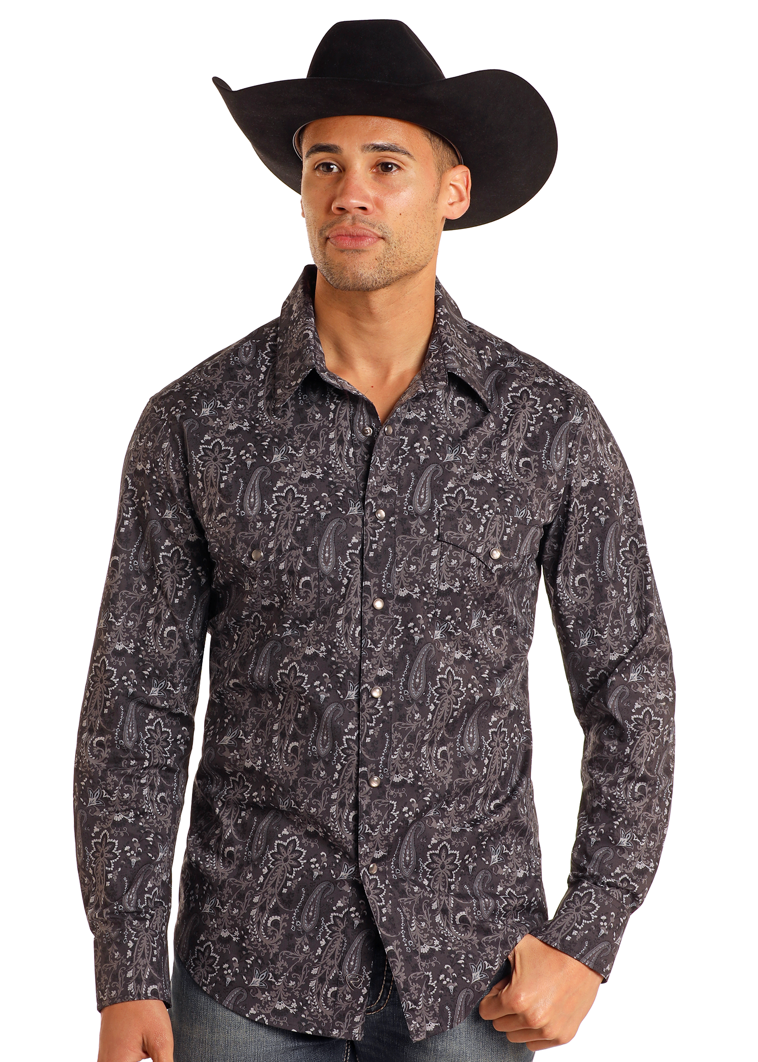 A man wearing a large black cowboy hat, blue jeans, and a Rock & Roll Denim Slim Fit Black Paisley Print Long Sleeve Snap Shirt stands against a plain white background.