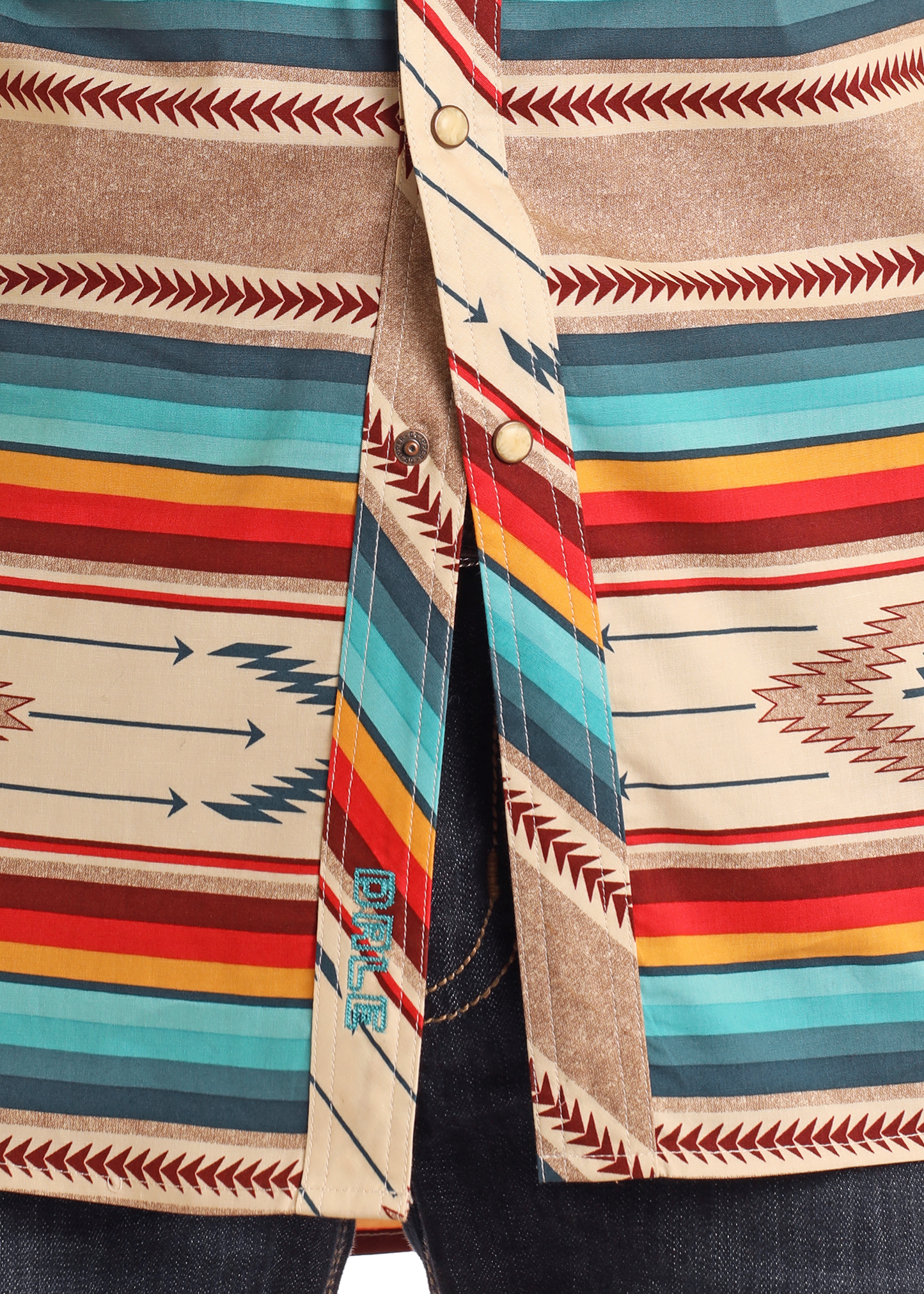 Close-up of the Rock & Roll Denim Dale Brisby Slim Fit Southwestern Serape Long Sleeve Snap Shirt, featuring a colorful red, teal, orange, and beige geometric pattern. The shirt is partially unbuttoned at the bottom, showing blue jeans underneath.