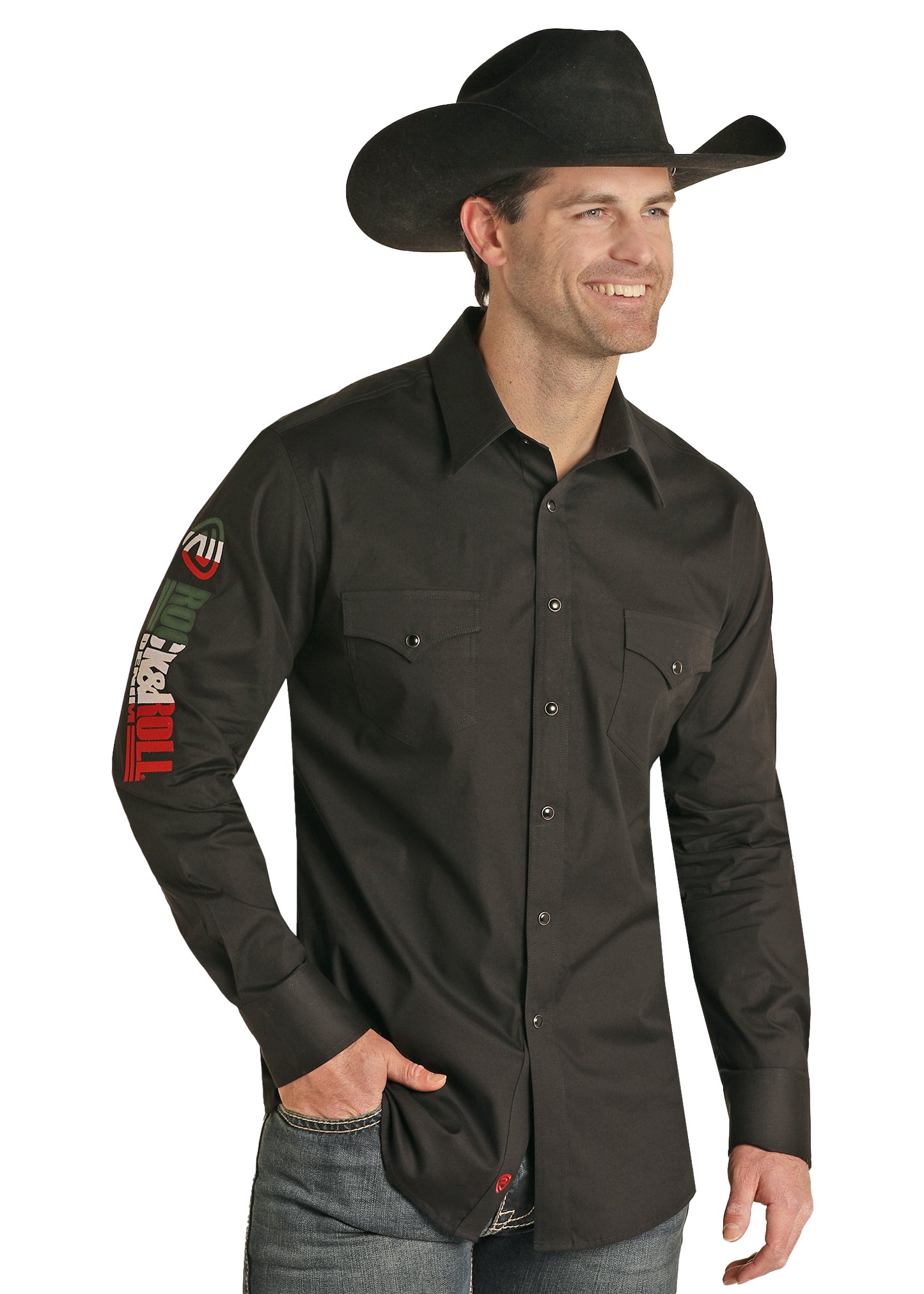 A smiling man in a black Rock & Roll Denim Slim Fit Logo Long Sleeve Snap Shirt with colorful right sleeve patches and a black cowboy hat stands with one hand in his jeans pocket against a white background.