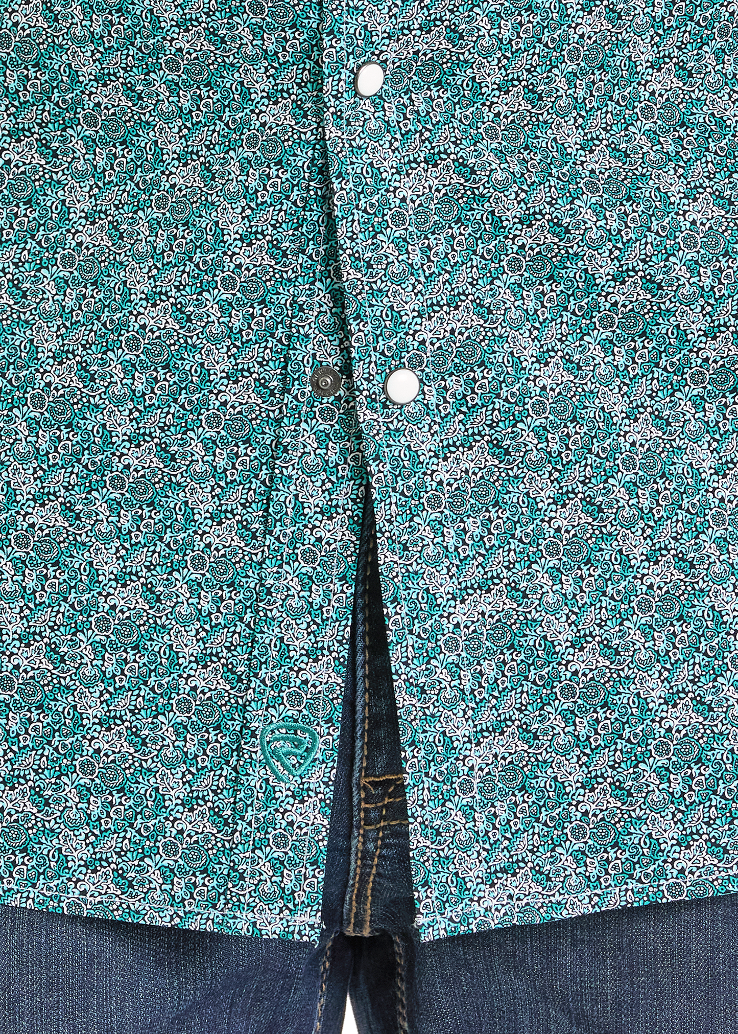 Close-up of the Rock & Roll Denim Slim Fit Turquoise Floral Long Sleeve Snap Shirt, showcasing its teal and white floral pattern and pearl snaps, partially unbuttoned at the bottom to reveal blue jeans underneath.