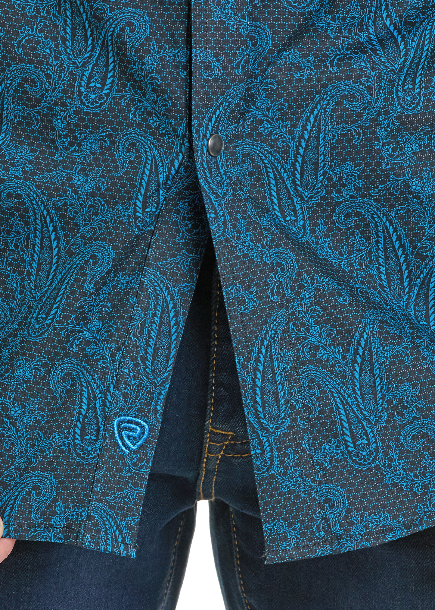 Close-up of the Rock & Roll Denim Slim Fit Dark Paisley Long Sleeve Snap Shirt, partly unbuttoned at the bottom to show dark denim jeans. A small blue embroidered logo accents the hem.