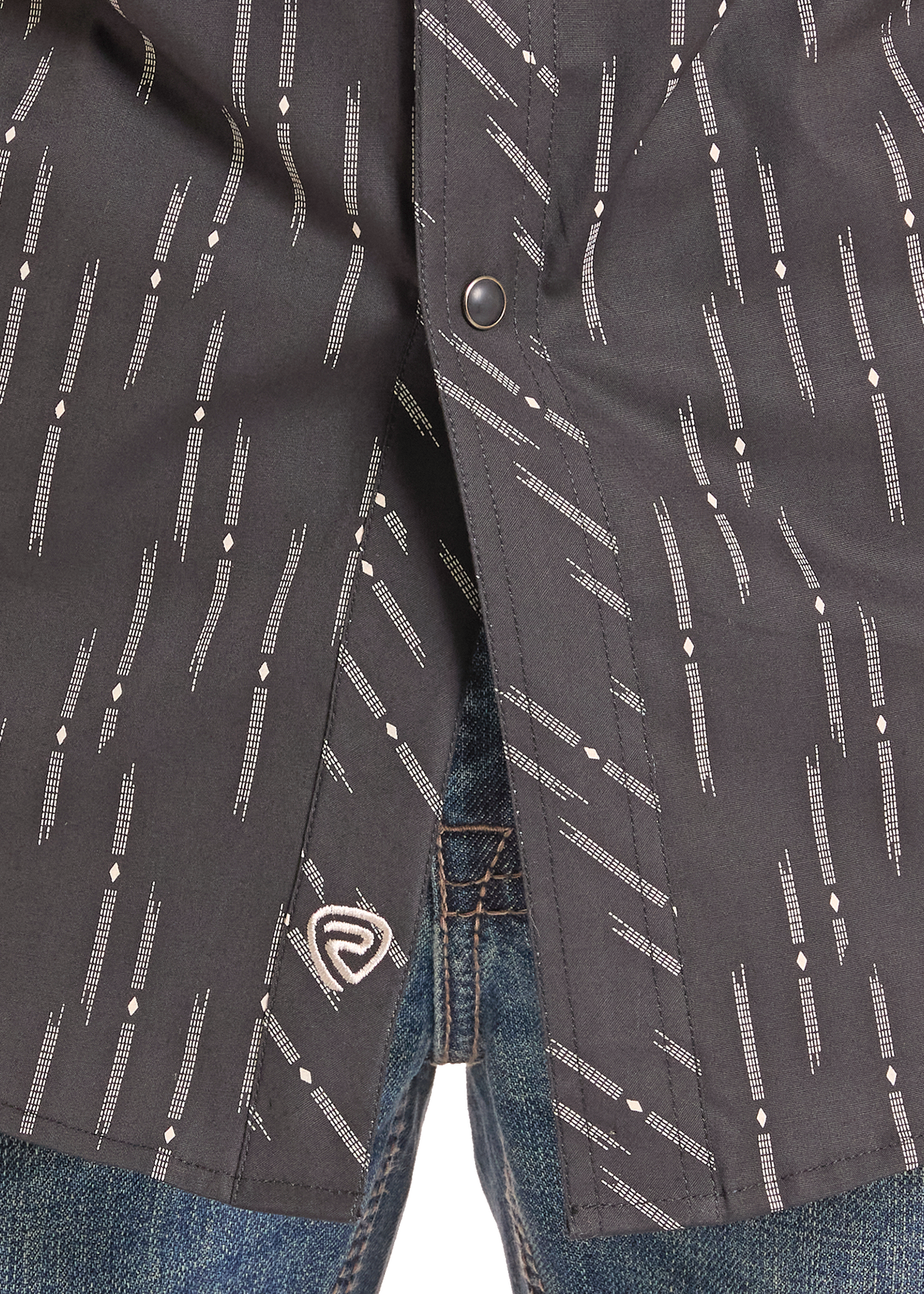 Close-up of a dark charcoal gray button-up shirt with a white geometric dash pattern, worn open over blue jeans.