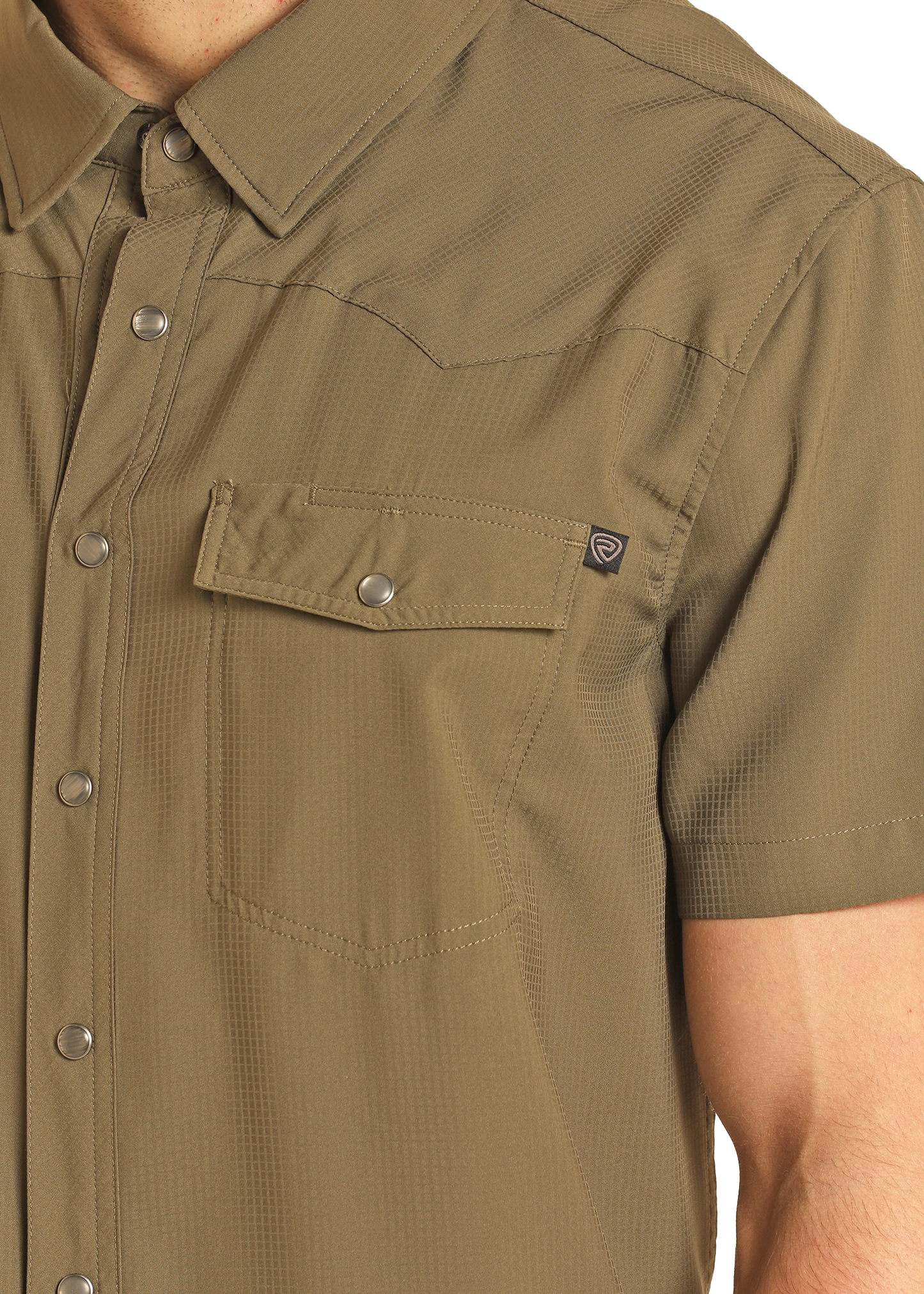 A close-up of a person wearing the Rock & Roll Denim TEK Western Olive Short Sleeve Shirt, showing snap buttons, a flap chest pocket, moisture-wicking fabric, and UPF 50 protection. Only the upper torso and part of the right arm are visible.