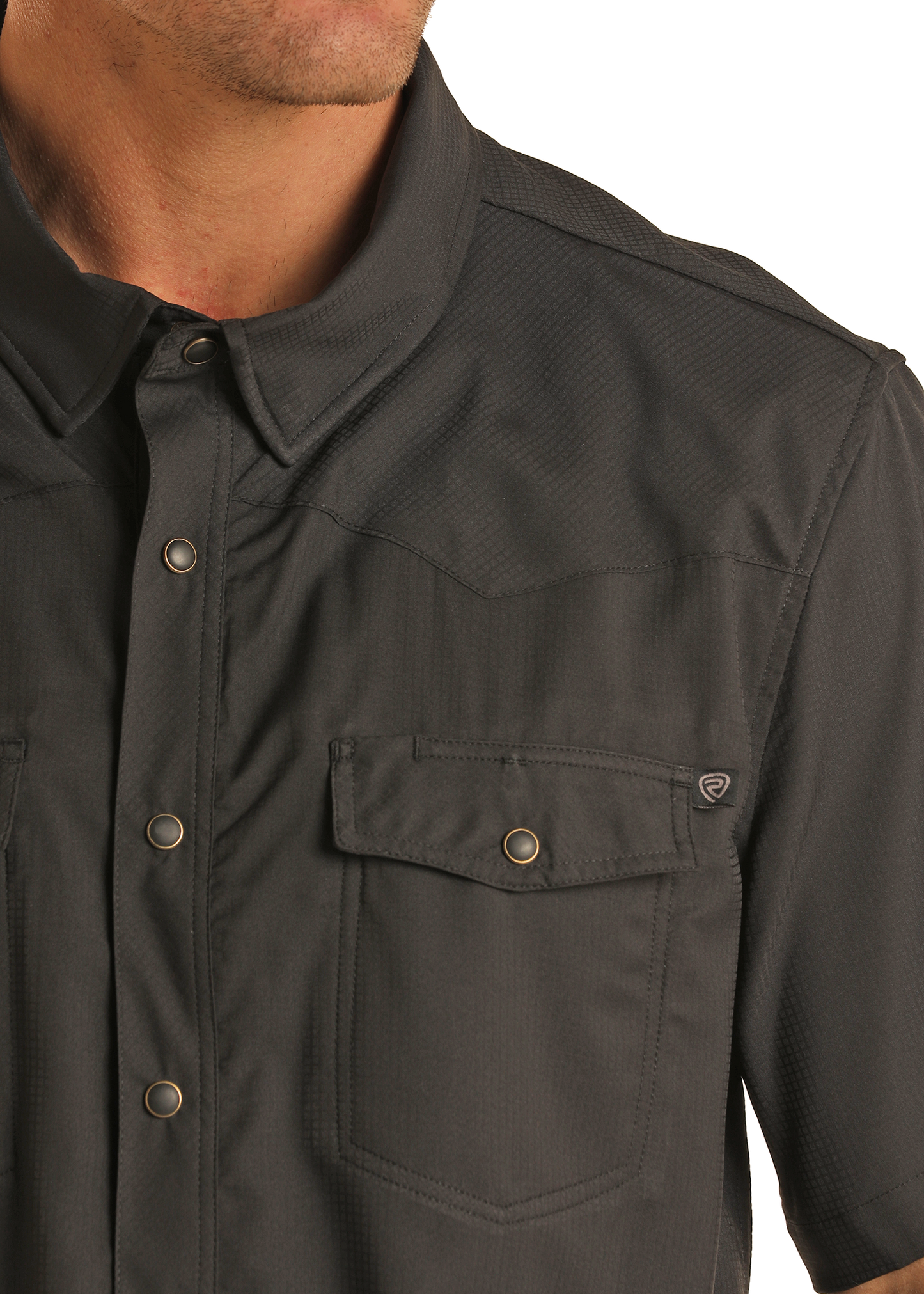 A close-up shows a person wearing the Rock & Roll Denim TEK Western Black Short Sleeve Shirt, featuring metal snaps and a front chest pocket. Only the lower half of their face and upper torso are visible.