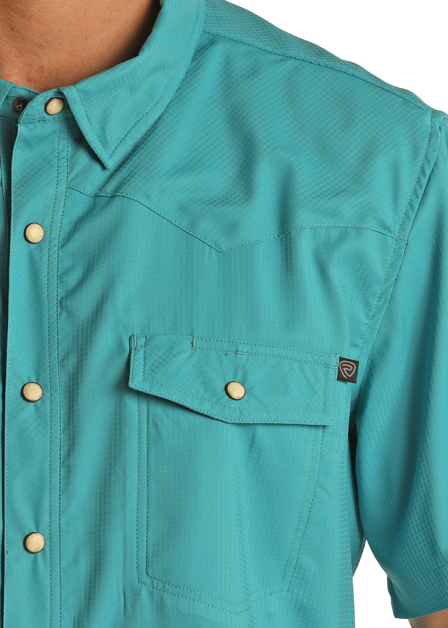 Close-up of the Rock & Roll Denim TEK Western Turquoise Short Sleeve Shirt, featuring beige snap buttons, a flap chest pocket, and a small black logo tag on the sleeve. Only part of the upper body is visible.