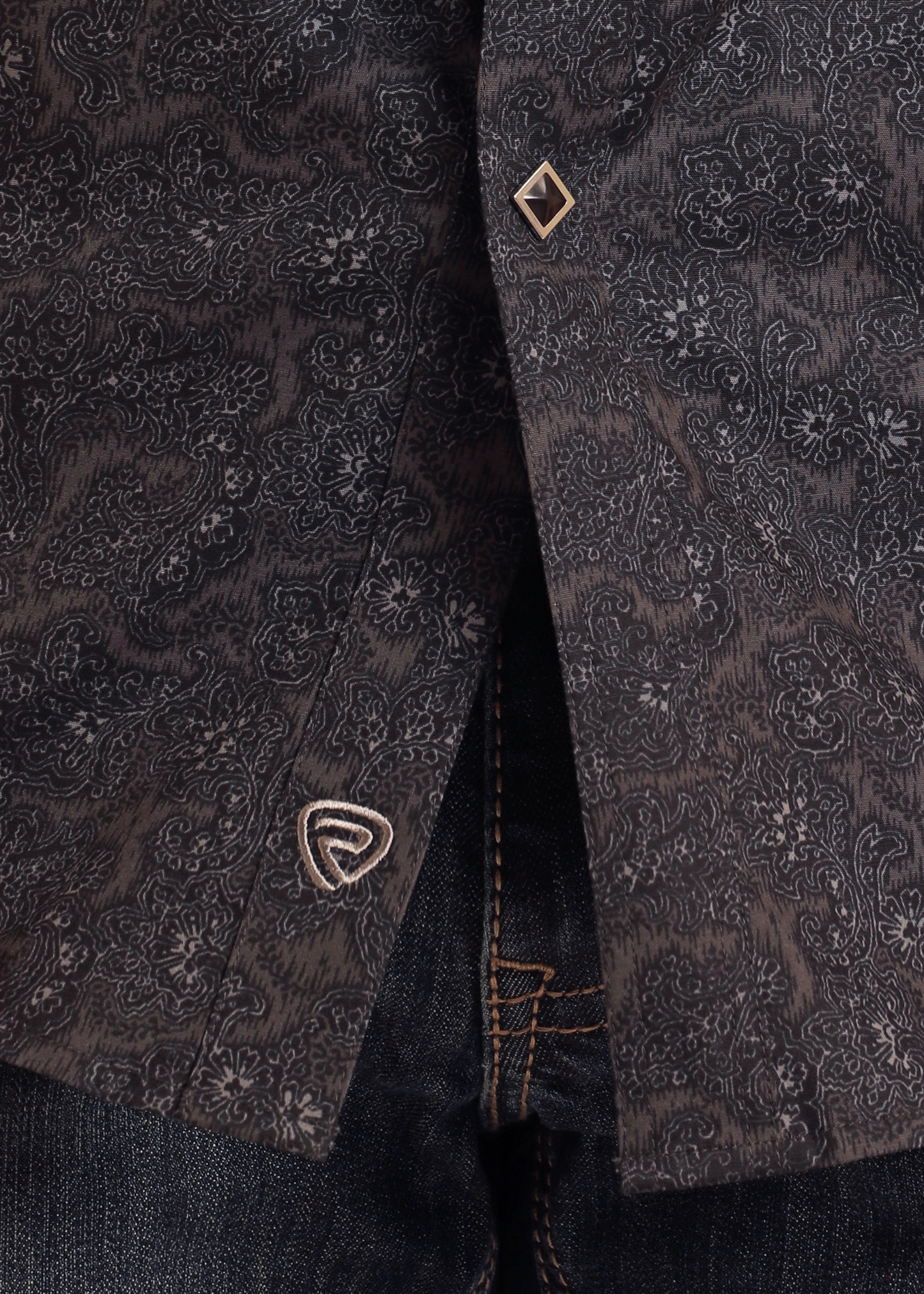 A close-up of the Rock & Roll Denim Slim Fit Black Paisley Short Sleeve Snap Shirt (S), partially unbuttoned to show blue denim jeans. The shirt features decorative metal snaps and an embroidered logo near the hem.