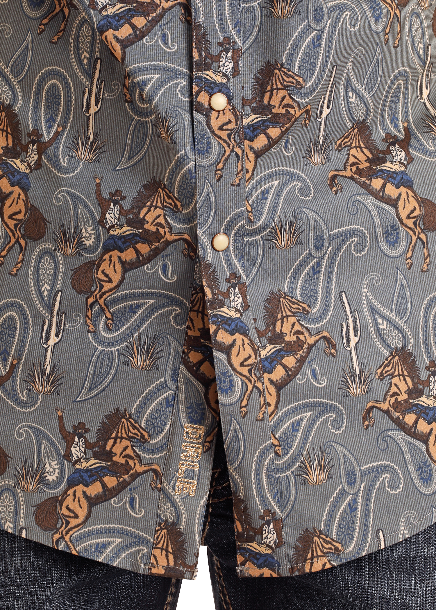 Closeup of the Rock & Roll Denim Dale Brisby Slim Fit Cowboy Print Short Sleeve Snap Shirt, featuring rodeo cowboys, bucking horses, cacti, paisley in blue, brown, and tan tones with pearl snaps; denim jeans are visible at the bottom.